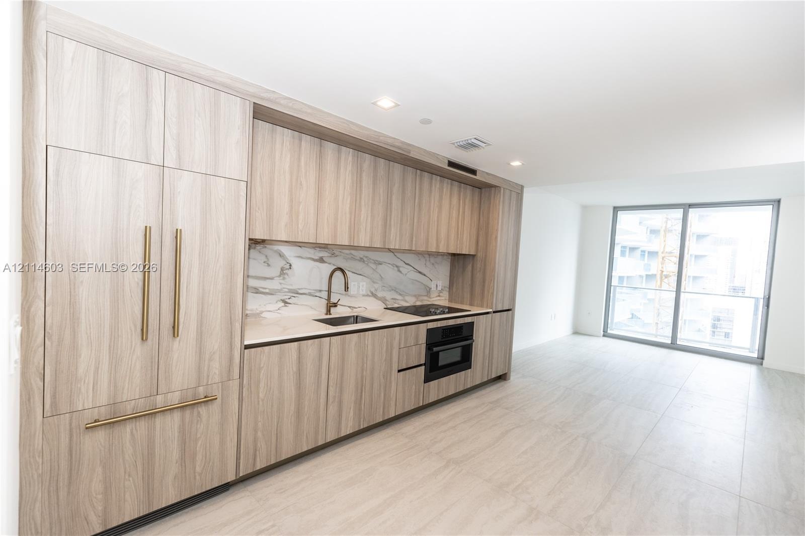 Contemporary kitchen featuring wood-finish cabinetry, integrated refrigerator, stone-patterned backsplash, recessed lighting, and large format tile fl