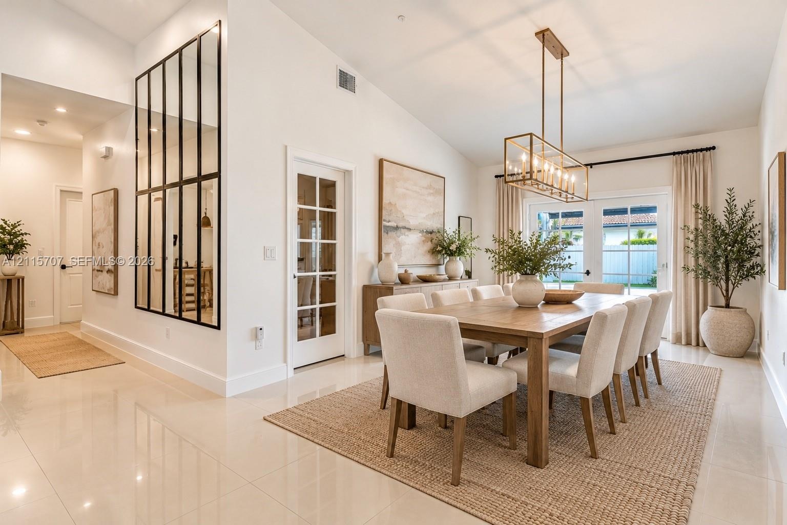 Vaulted ceilings, large-format tile flooring, metal-framed decorative mirror, glass-paneled interior door, and rectangular metallic chandelier