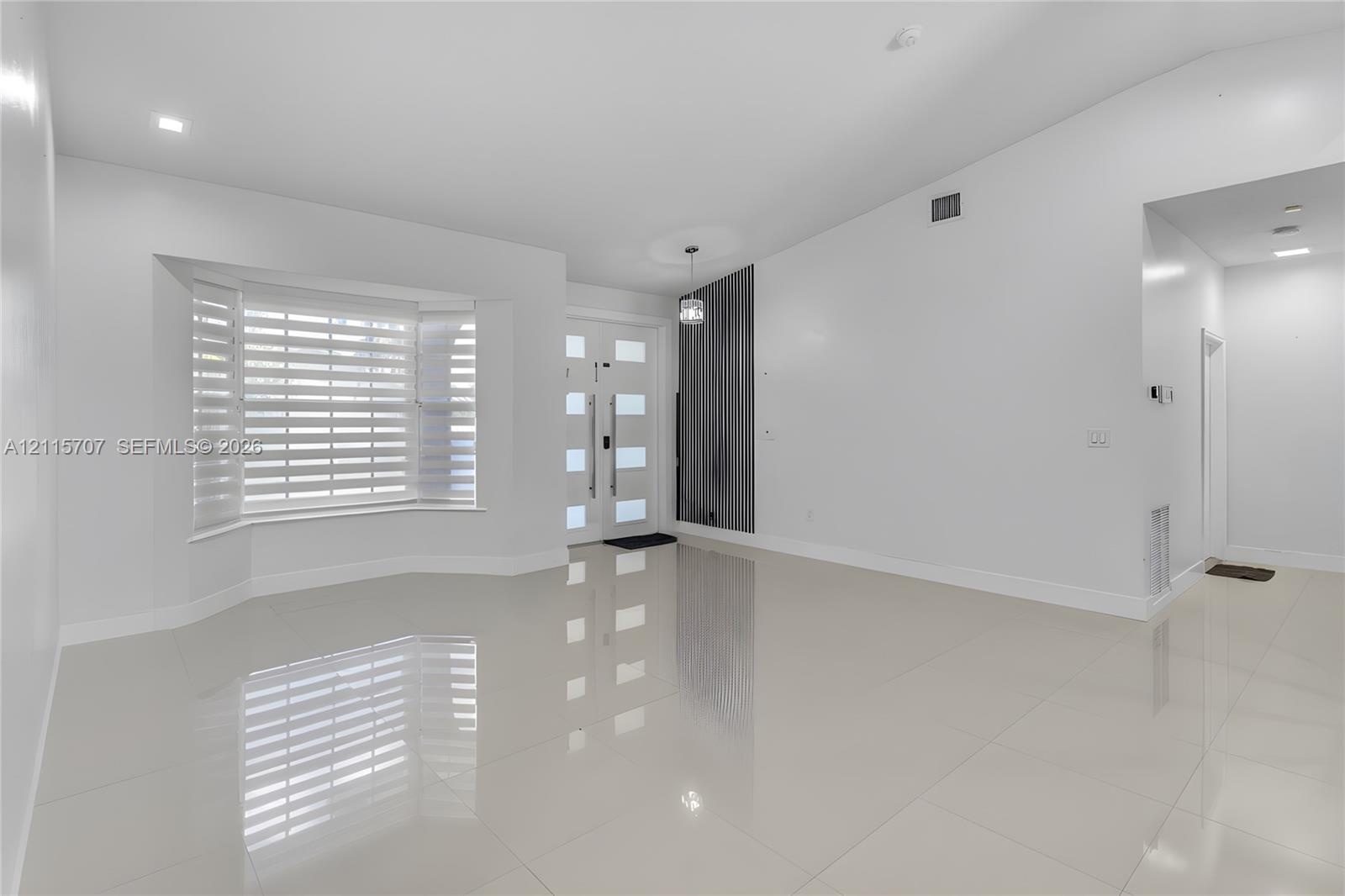 Bright interior featuring vaulted ceilings, polished tile flooring, a multi-pane front entry door with vertical handle hardware, and a bay window equi