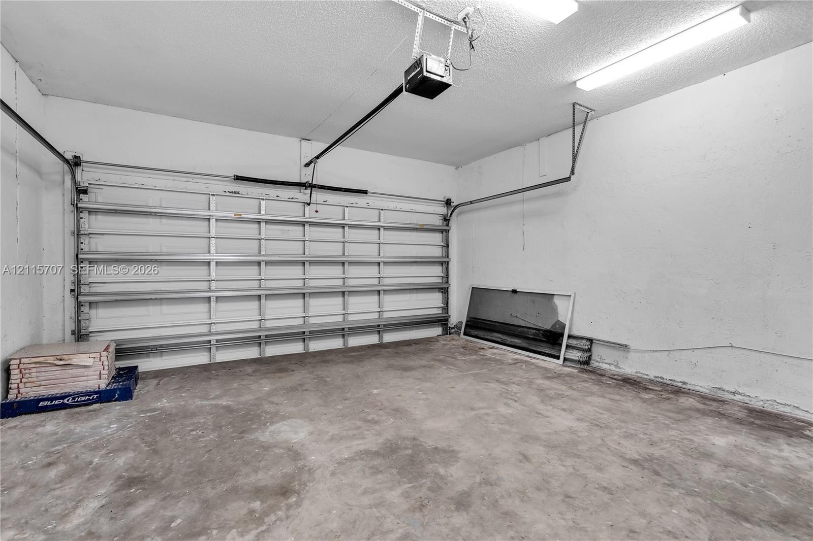 Attached garage featuring concrete flooring, an automated overhead door system, and ceiling-mounted fluorescent lighting