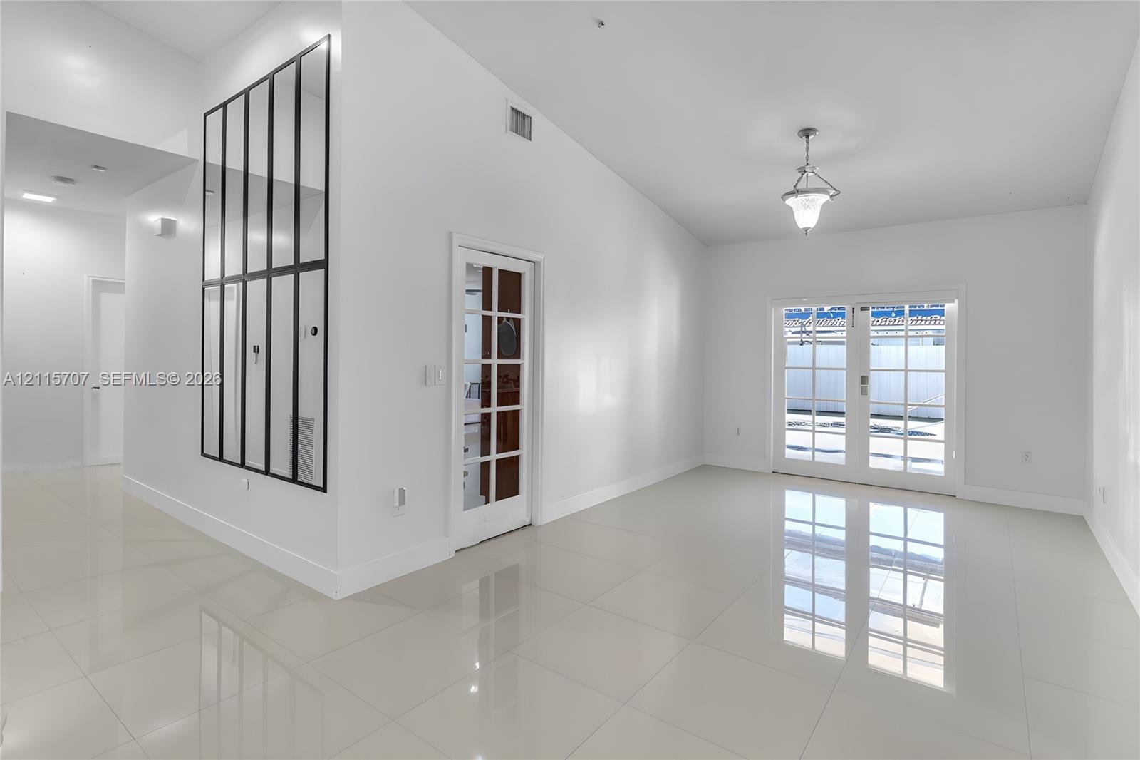Vaulted ceiling, neutral large-format tile flooring, decorative grid-pattern wall mirror, glass-paned interior door, and double glass-paned exterior d