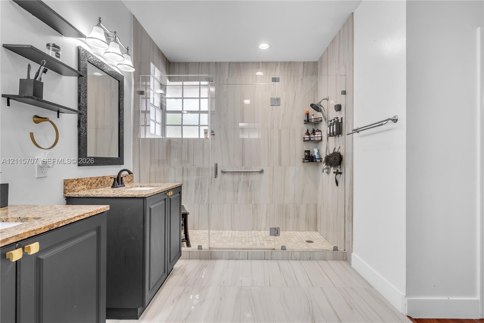 Bathroom featuring a dark wood-finish vanity with stone-surfaced countertop, walk-in shower with floor-to-ceiling tile, glass enclosure, and glass blo