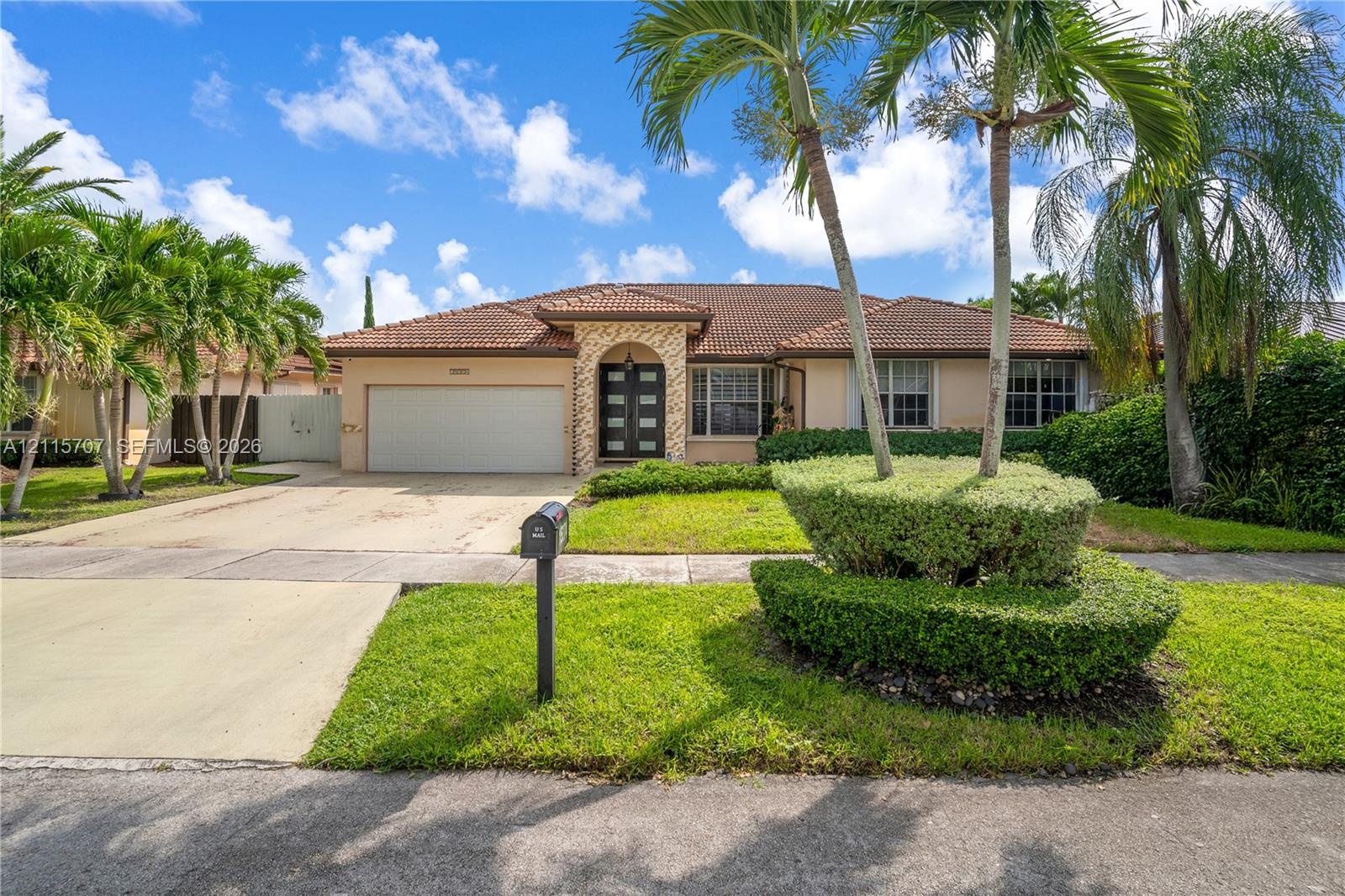 Single-story residence featuring a tile roof, decorative stone entryway facade, multi-panel glass front door, two-car garage, and mature landscaping