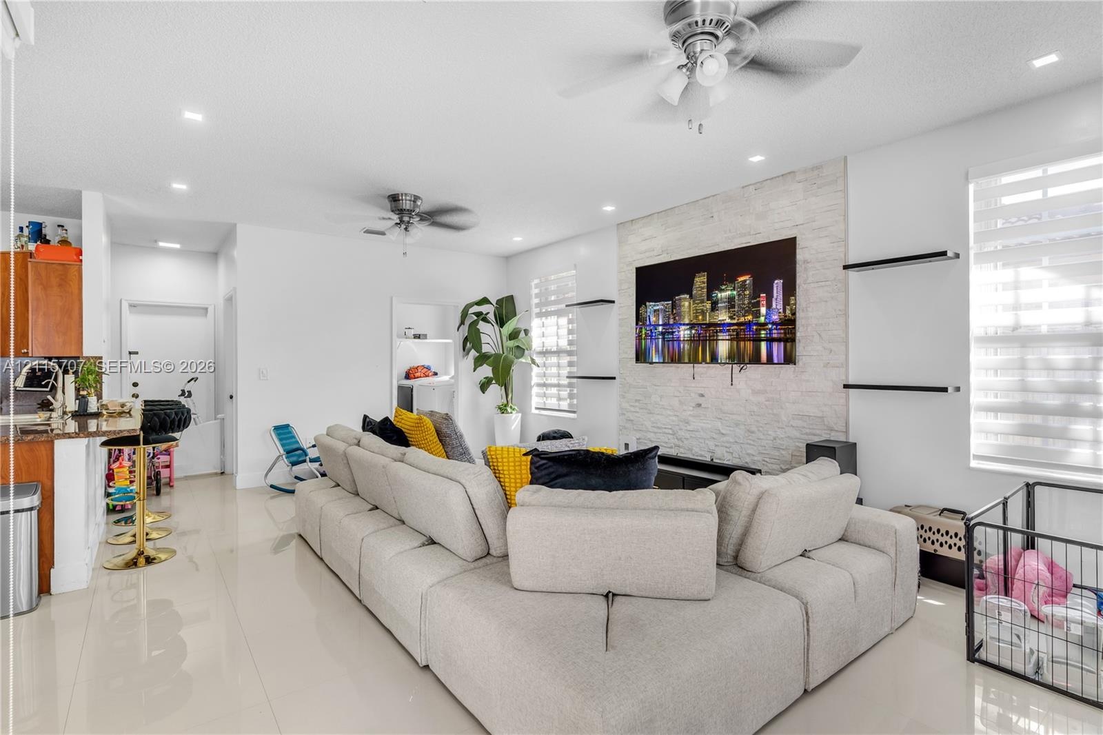 Living area featuring a floor-to-ceiling natural stone veneer accent wall, recessed lighting, ceiling fans, large-format tile flooring, and integrated