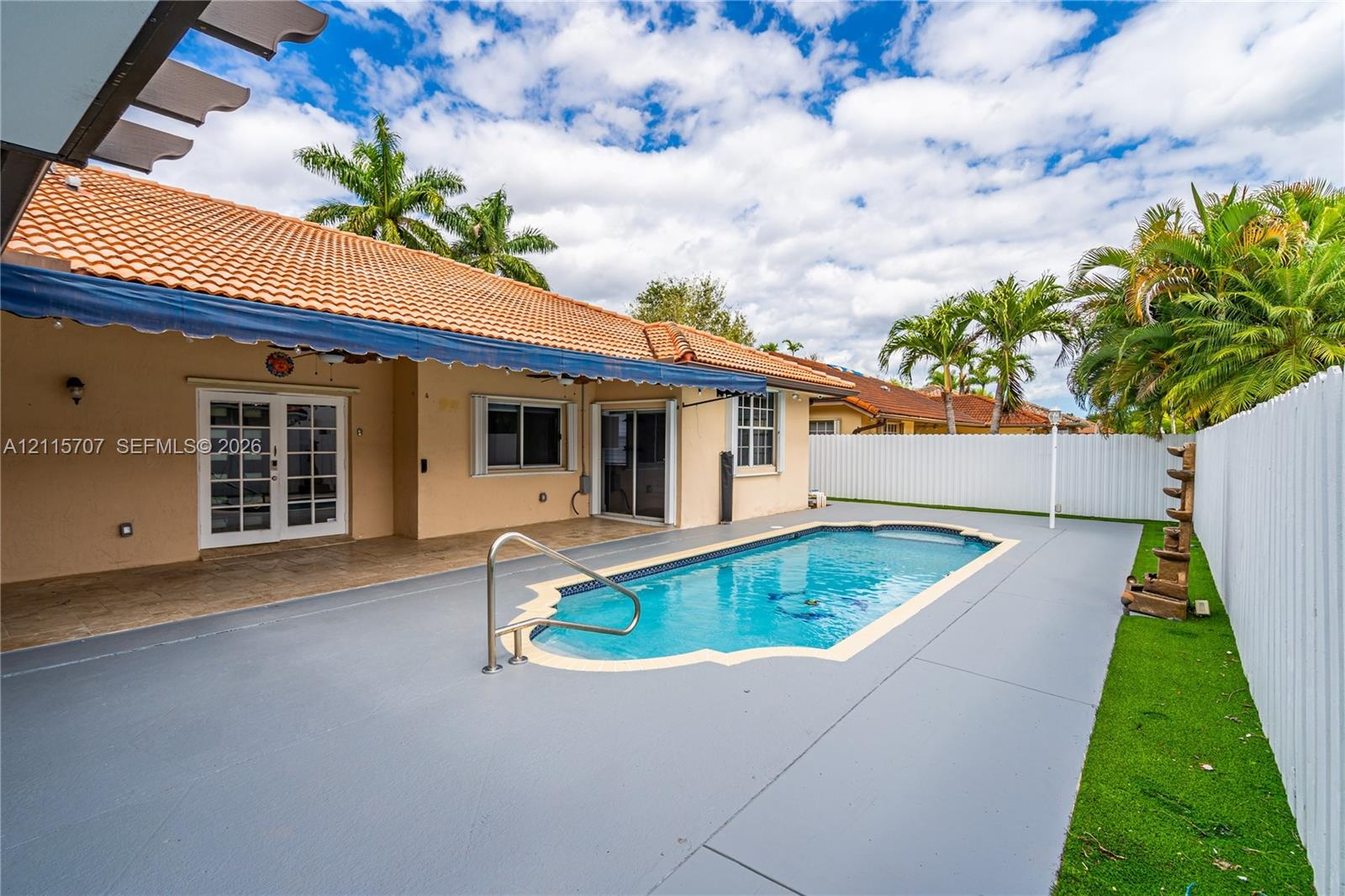 In-ground pool with stone coping, covered patio, tile roof, and enclosed privacy fencing