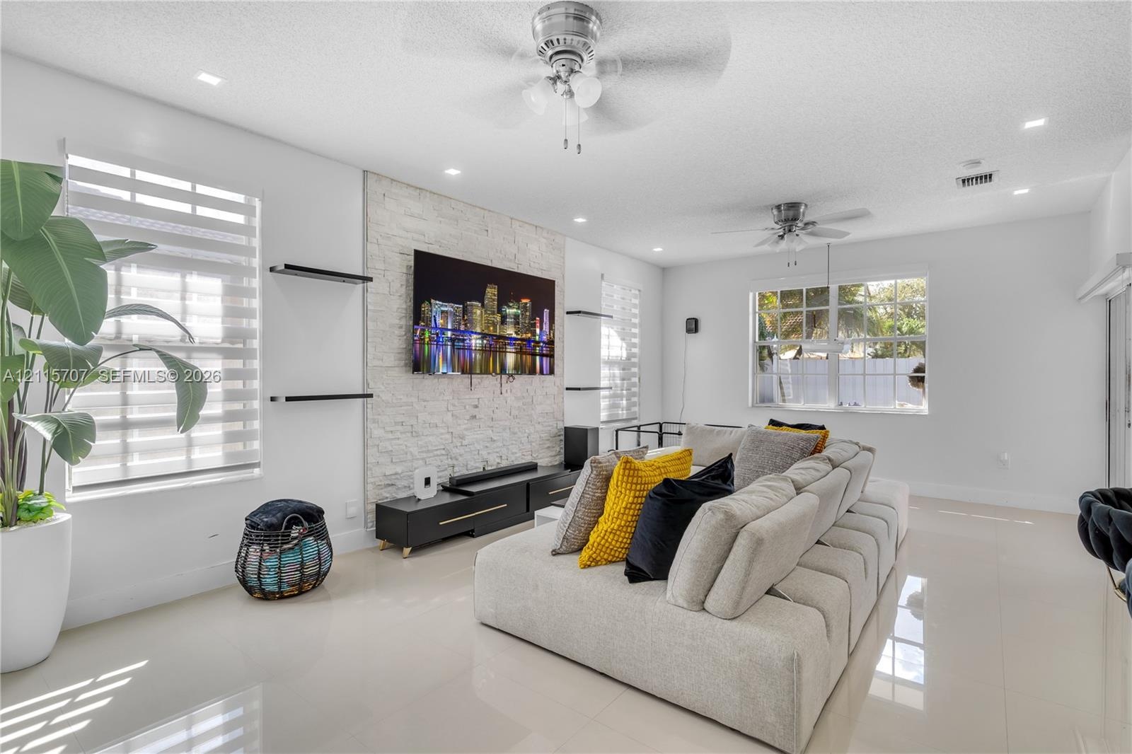 Living area featuring a floor-to-ceiling textured stone accent wall, large-format tile flooring, recessed ceiling lighting, and dual ceiling fans