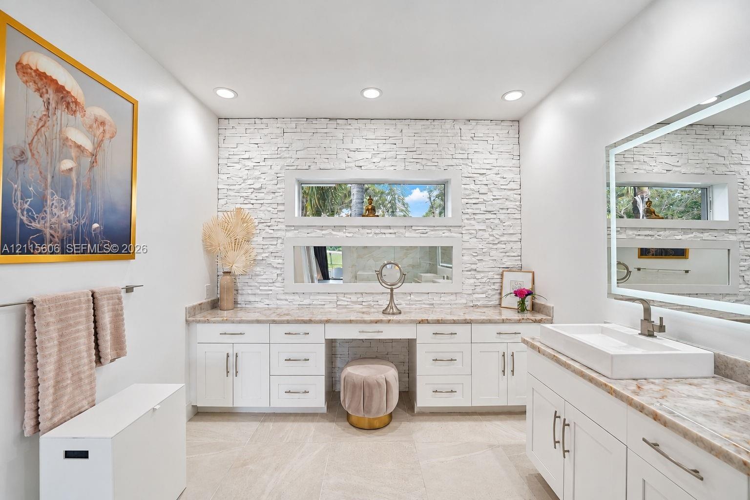 Stone-veneer feature wall with stacked horizontal windows, white cabinetry with integrated vanity, rectangular vessel sink, and illuminated vanity mir