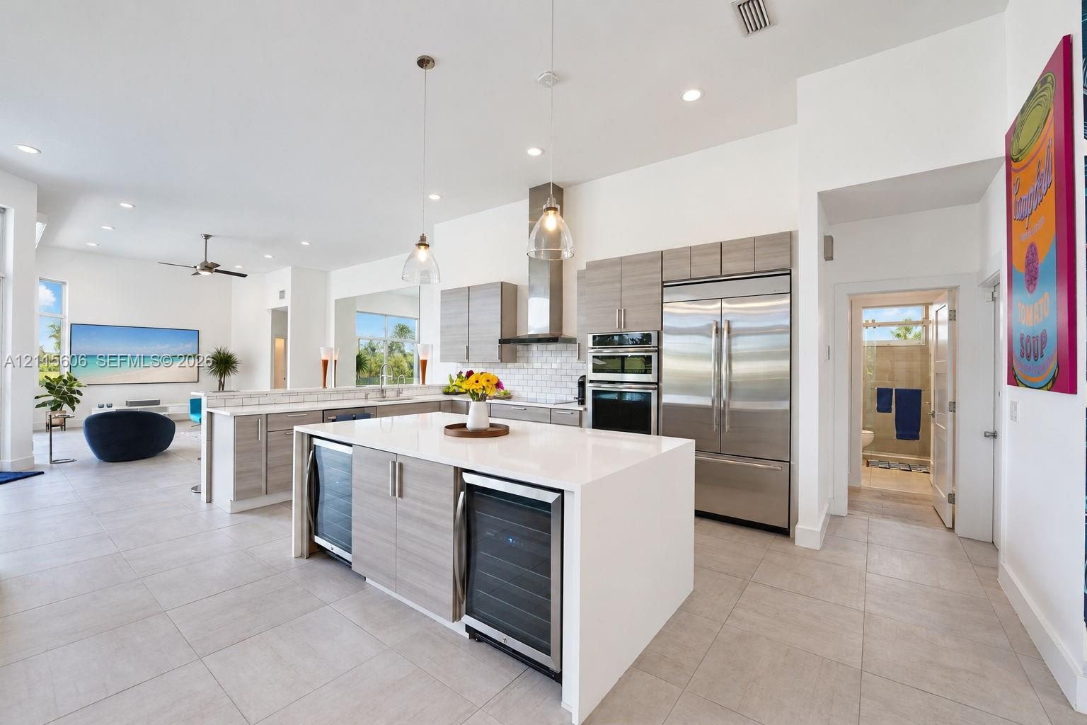 Kitchen featuring light-finish cabinetry, a large central island with a solid surface countertop, stainless steel appliances, dual beverage coolers, a