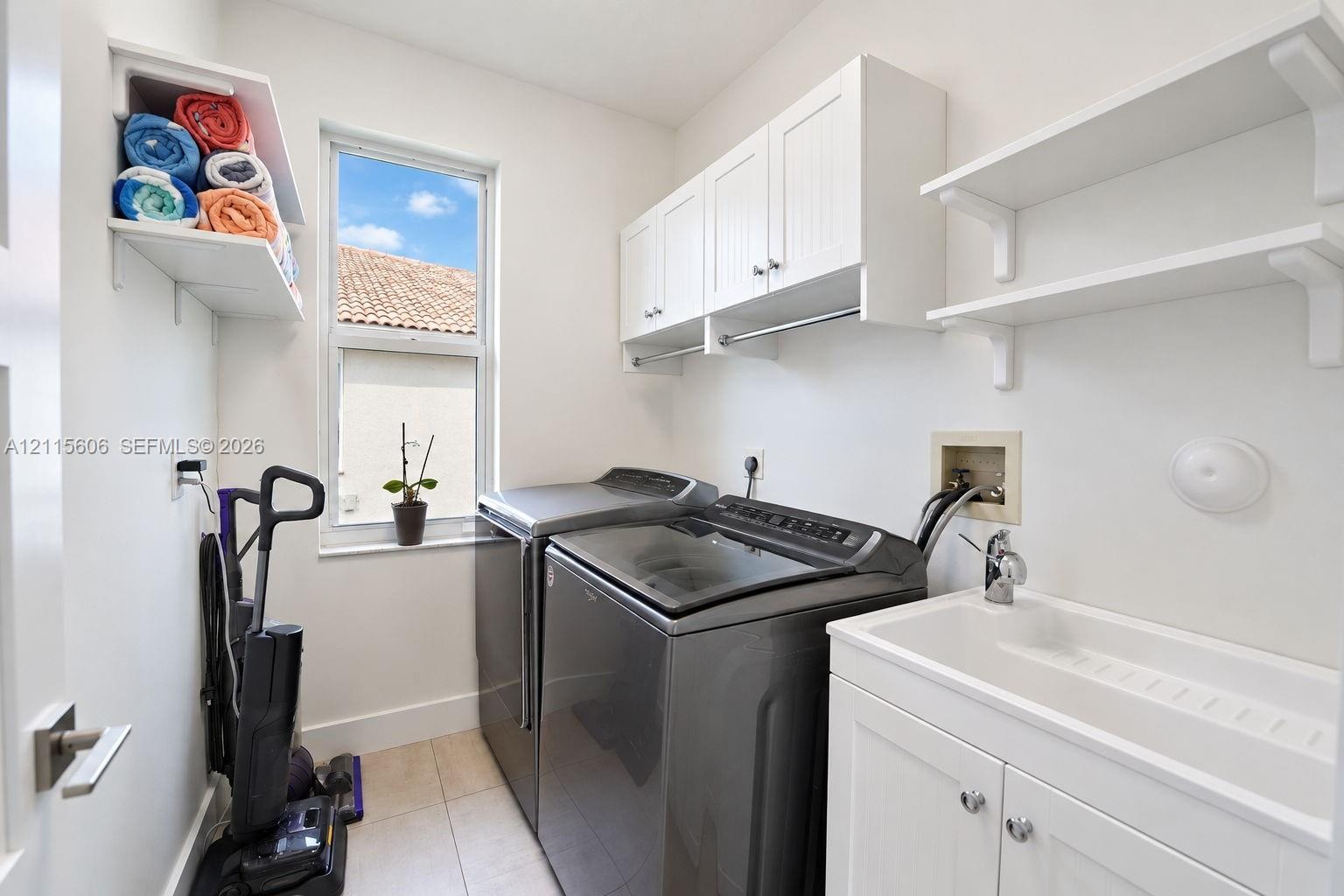 Laundry room featuring white shaker-style cabinetry, open wall shelving, a built-in utility sink with a chrome faucet, and tile flooring