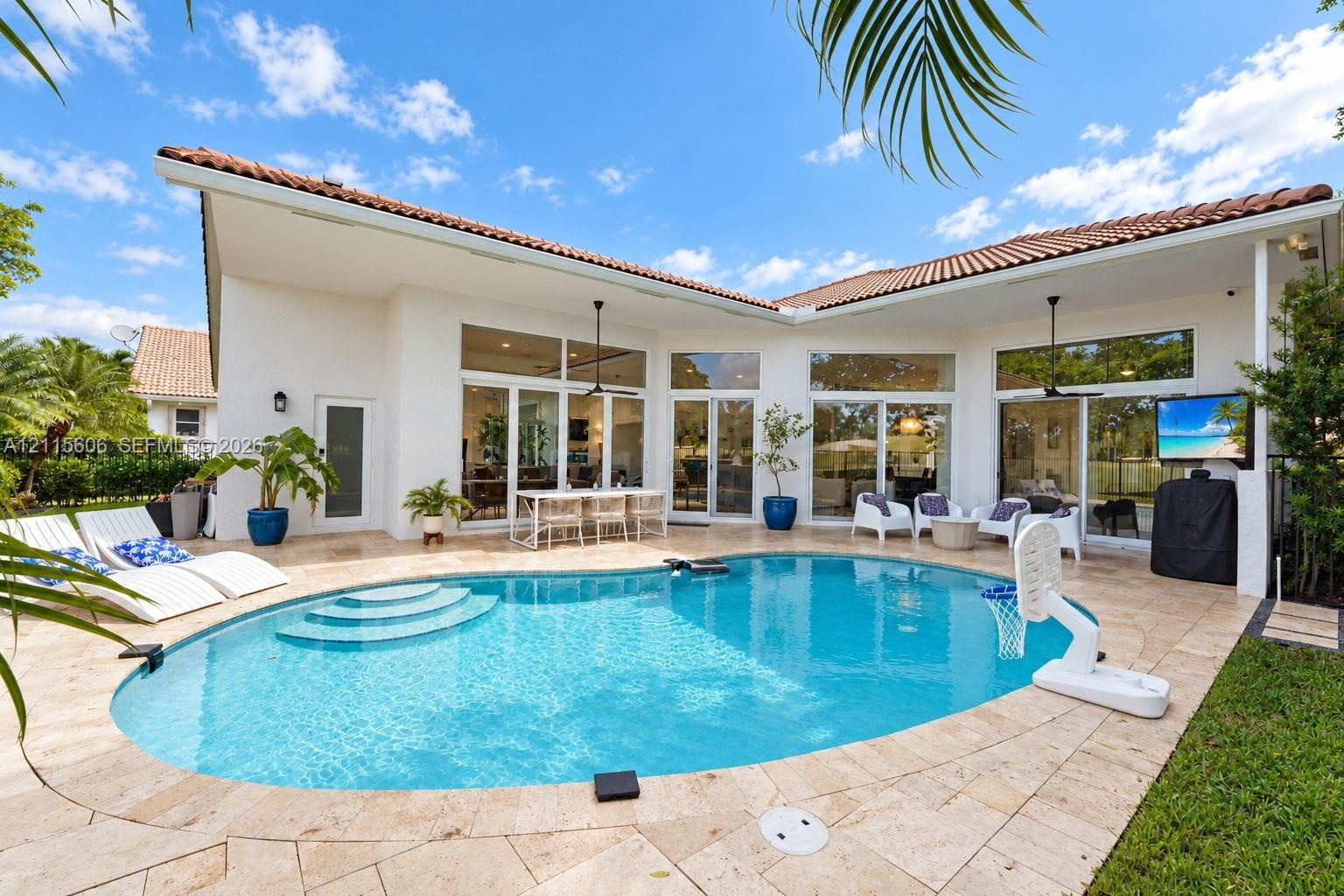 Outdoor living area featuring a custom-shaped swimming pool with built-in steps, expansive stone paver patio, covered loggia, and large-scale glass sl