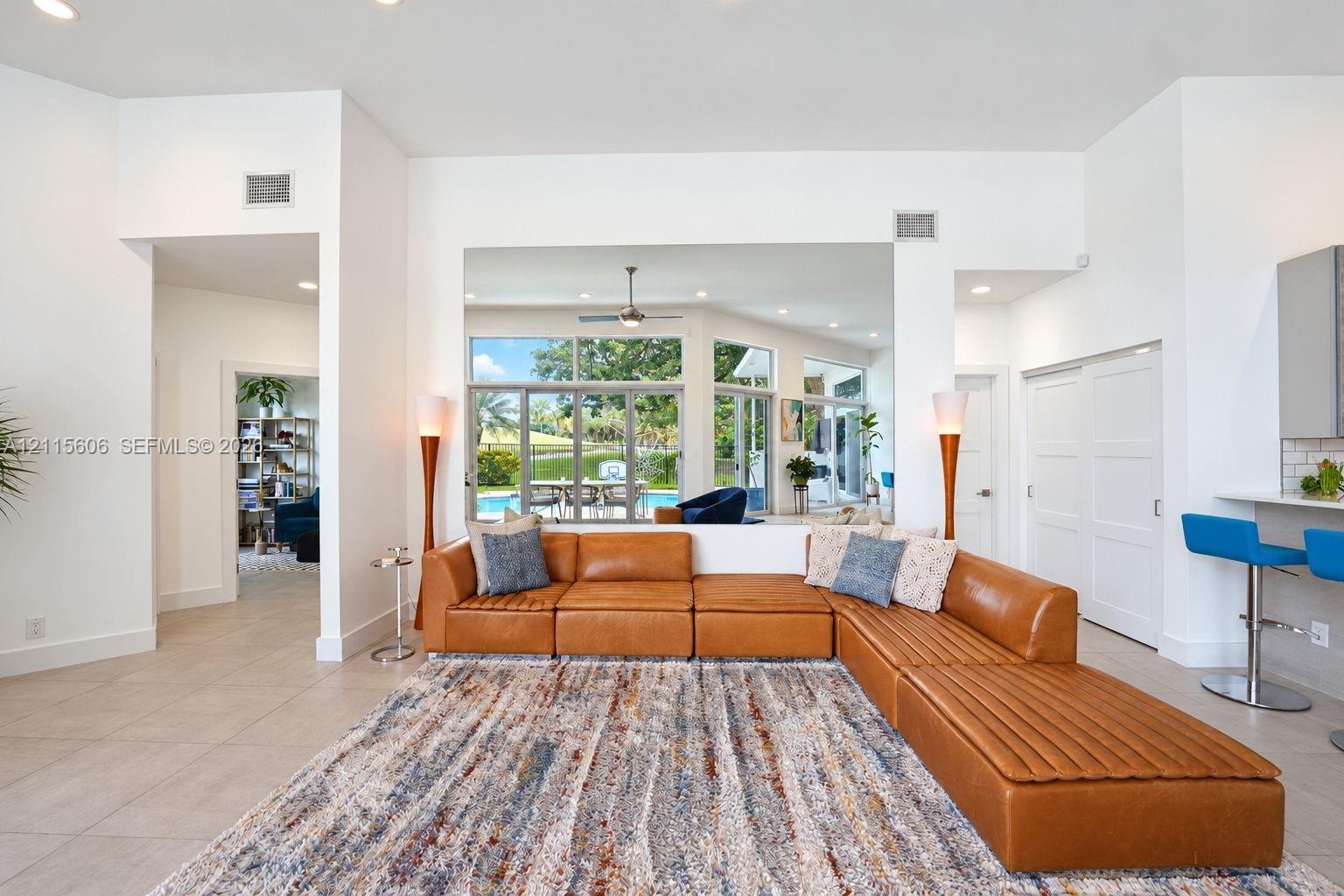 Open-concept interior featuring large-format tile flooring, recessed ceiling lighting, a ceiling fan, and sliding glass doors revealing an outdoor poo
