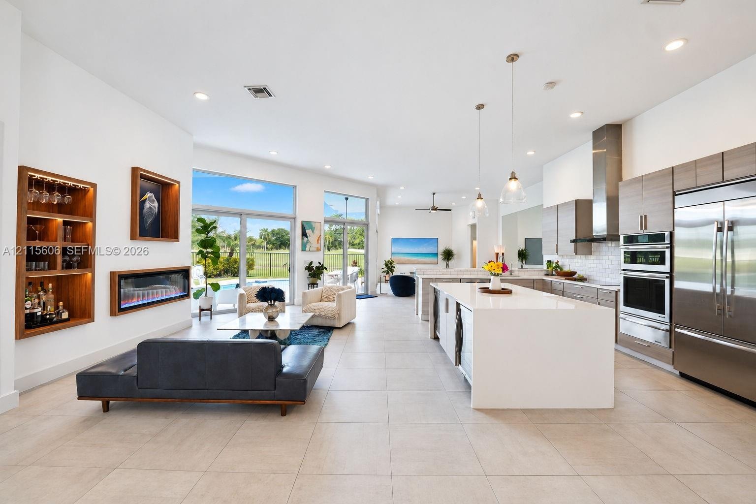 Open-concept living space featuring a central kitchen island with waterfall-edge stone countertop, built-in recessed shelving, integrated linear firep