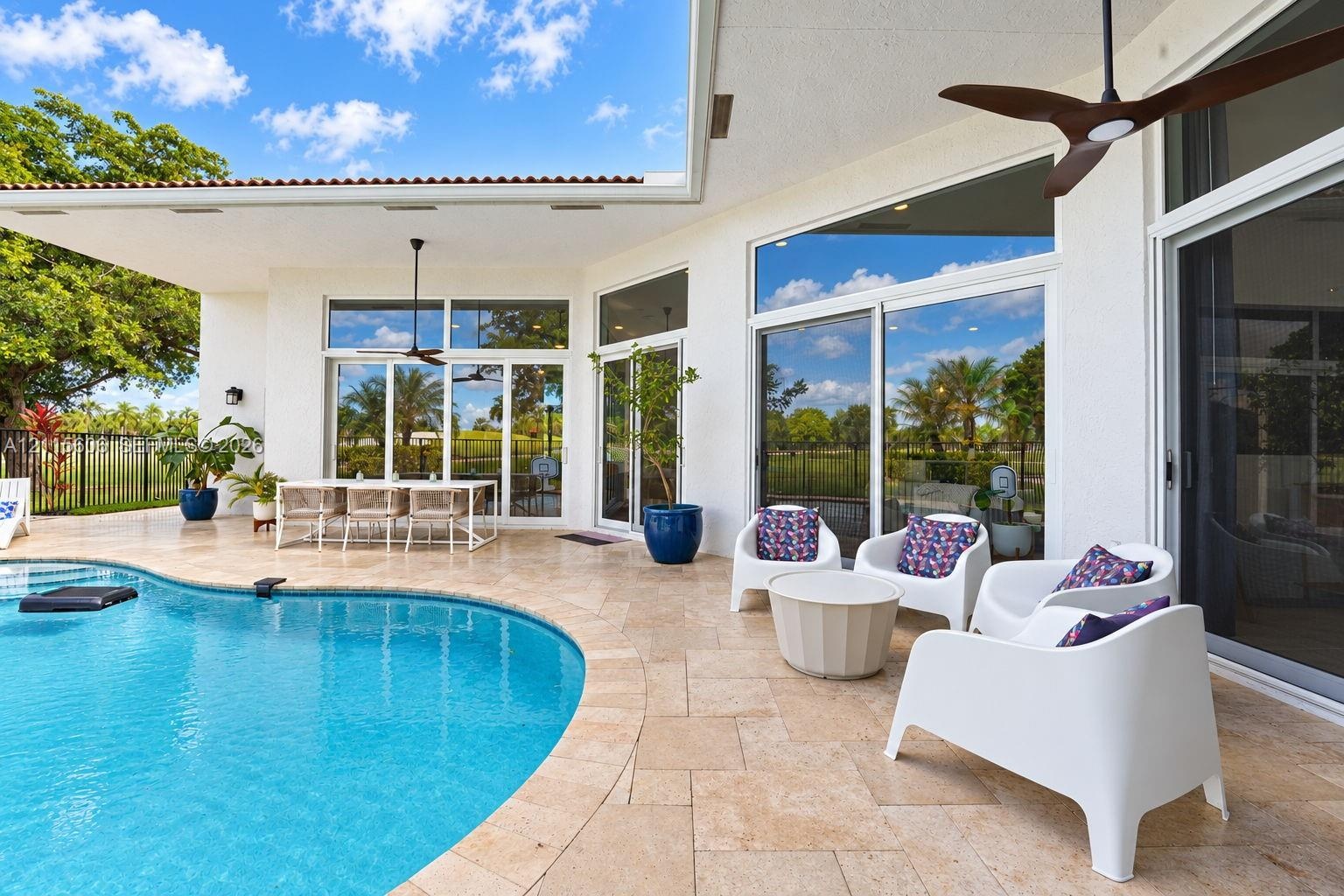 Covered patio featuring stone-tile flooring, ceiling fans, oversized glass sliding doors, and a curved swimming pool