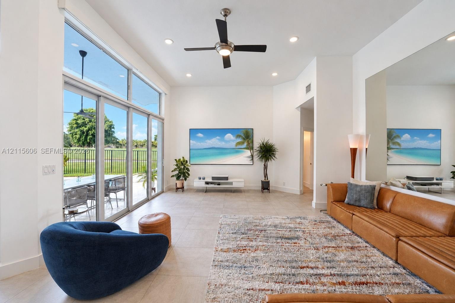 High-ceiling living space featuring floor-to-ceiling glass sliding doors, large-format tile flooring, a mounted ceiling fan with integrated lighting, 