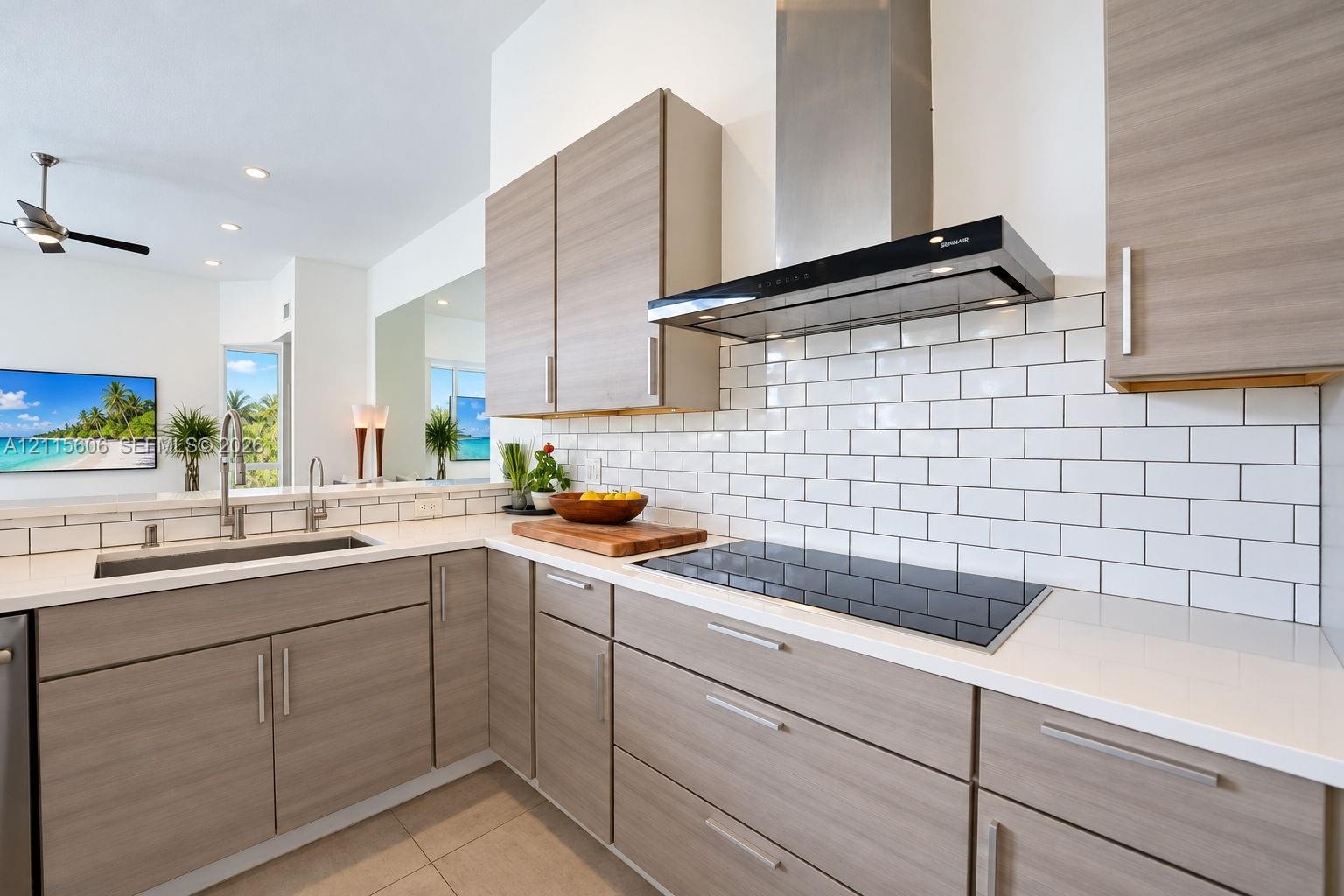 Kitchen featuring flat-panel wood-finish cabinetry, quartz countertops, white subway tile backsplash, stainless steel range hood, and integrated induc