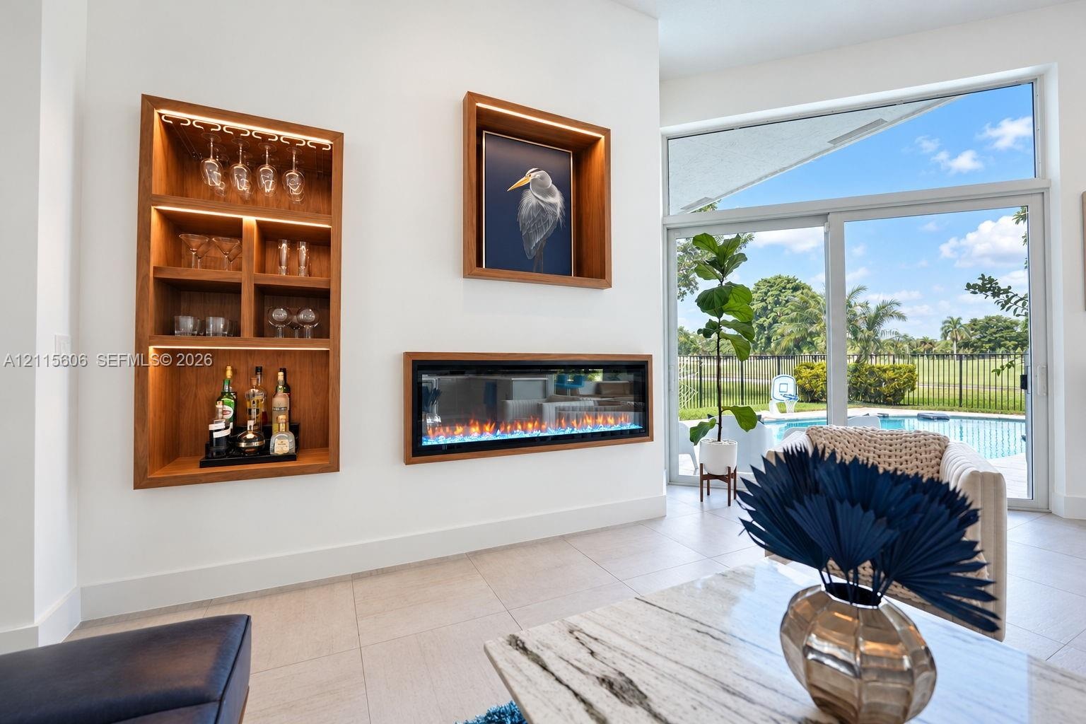 Built-in illuminated wood shelving, recessed linear electric fireplace, large-format tile flooring, and floor-to-ceiling sliding glass doors with outd