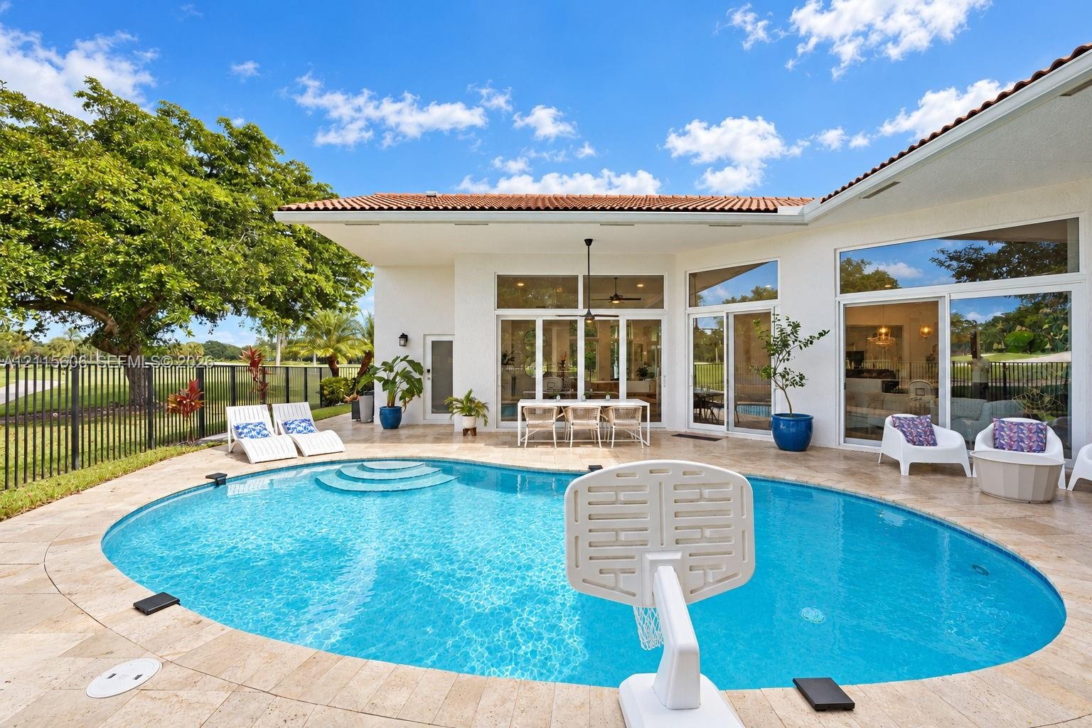 Outdoor patio featuring a travertine stone deck, a curved swimming pool with integrated steps, multiple floor-to-ceiling glass sliding doors, and a co