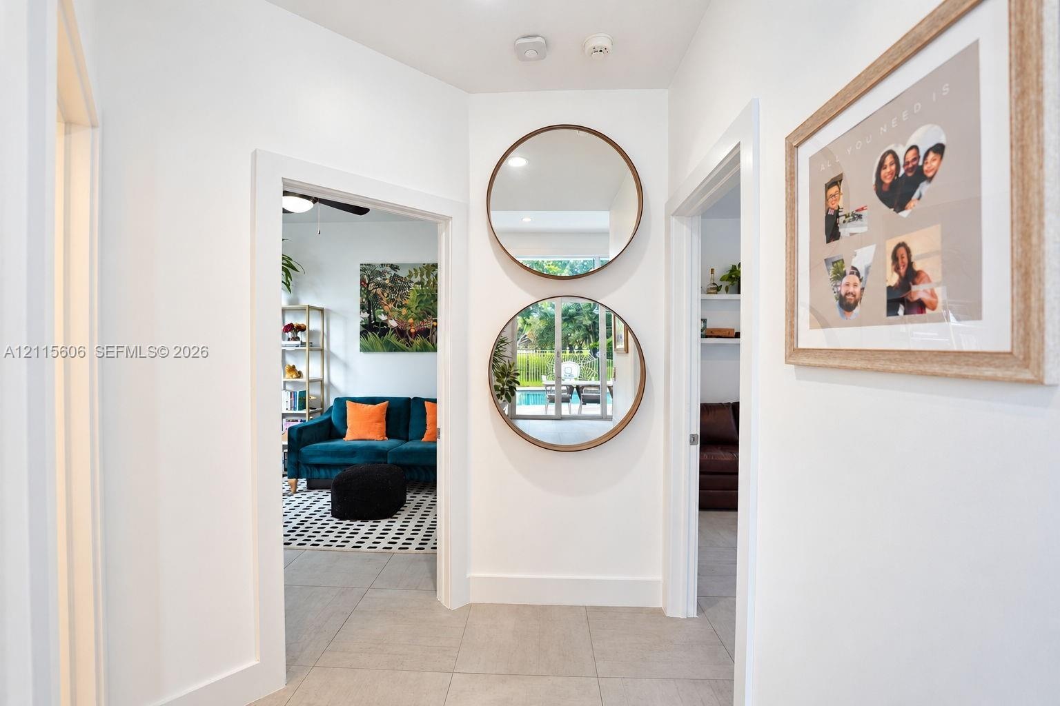 Interior hallway featuring large-format tile flooring, neutral wall finishes, and dual circular wall-mounted mirrors with wood-toned frames