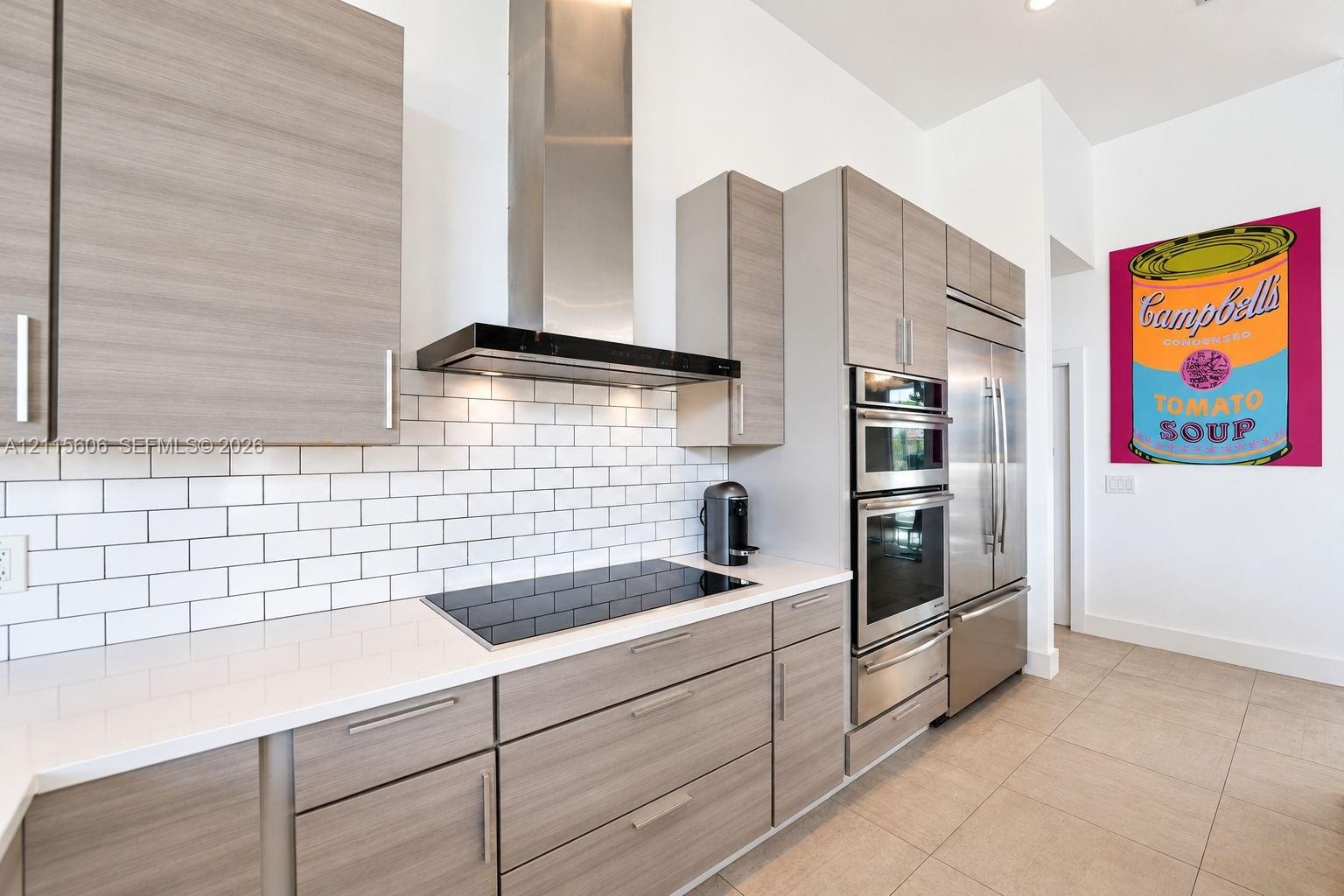 Kitchen featuring light wood-finish cabinetry, white solid-surface countertops, white subway tile backsplash, stainless steel built-in appliances, and