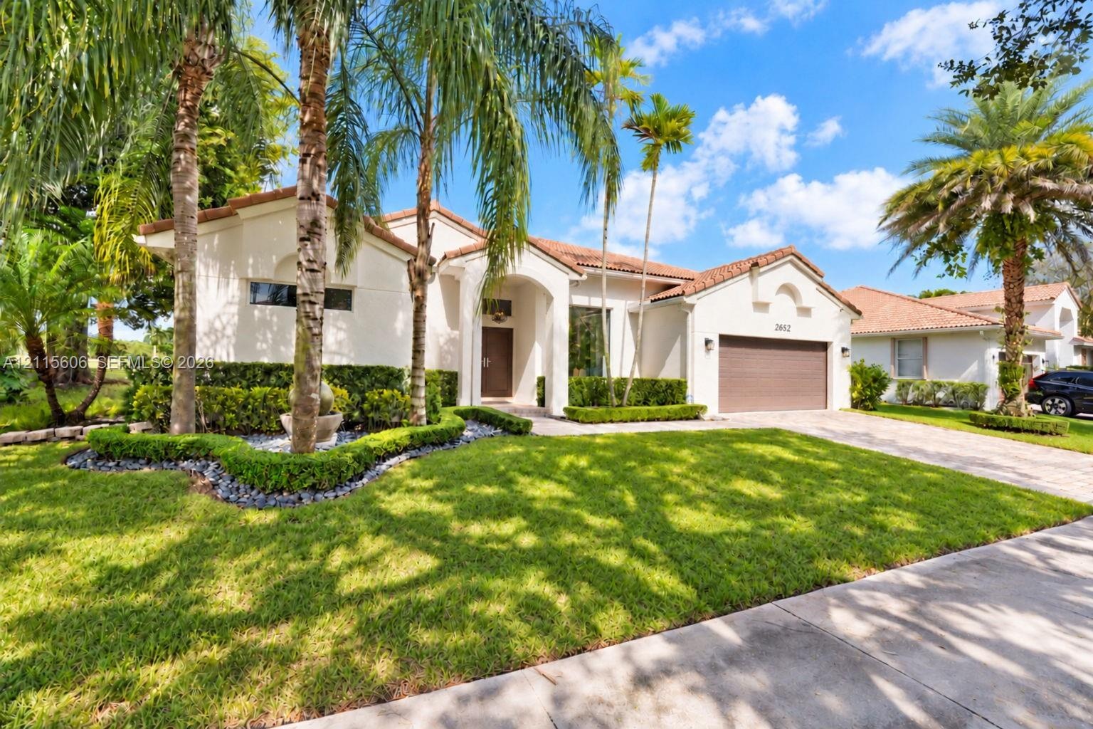 Stucco exterior featuring a clay tile roof, arched entryway, manicured hedges, and mature palm trees