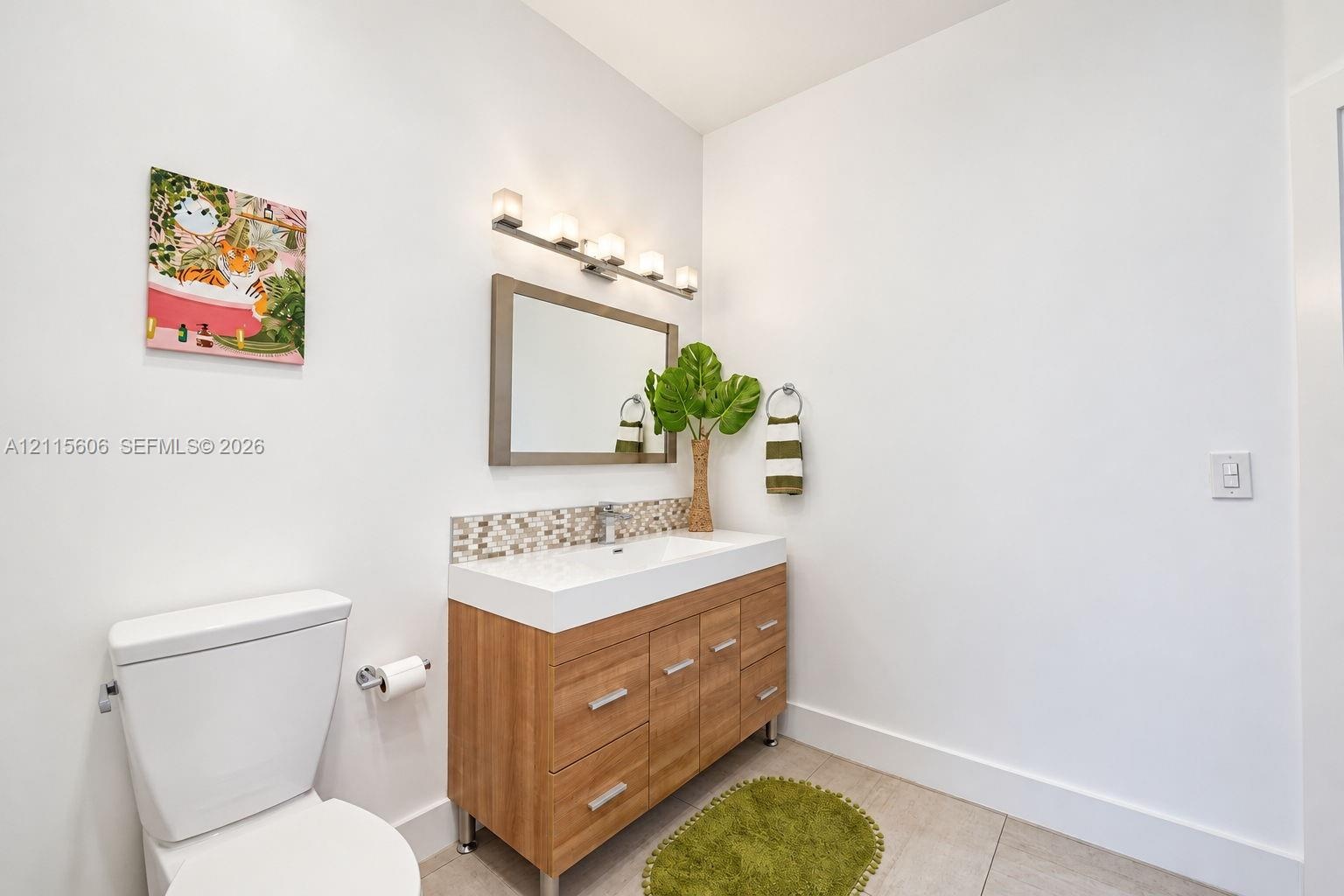Wood-finish vanity with a rectangular sink, multi-tone glass tile backsplash, framed wall mirror, and chrome multi-bulb light fixture