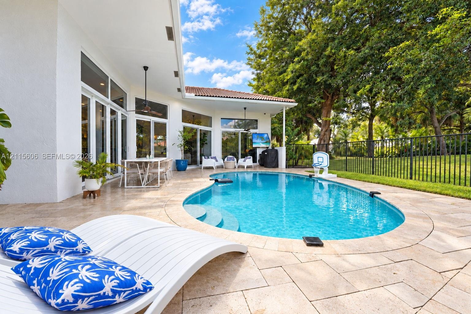 Outdoor patio featuring natural stone pavers, a custom-shaped swimming pool with integrated steps, a covered lanai with ceiling fans, and black metal 