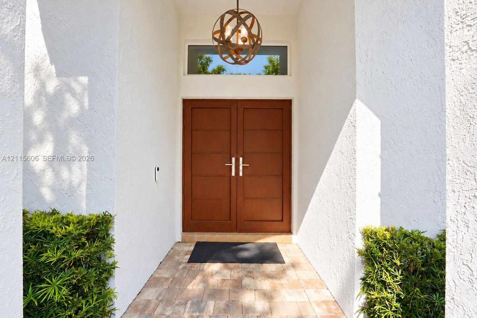 Entryway featuring double wood-finish doors with horizontal paneling, a circular metal orb pendant light fixture, a rectangular transom window, and st