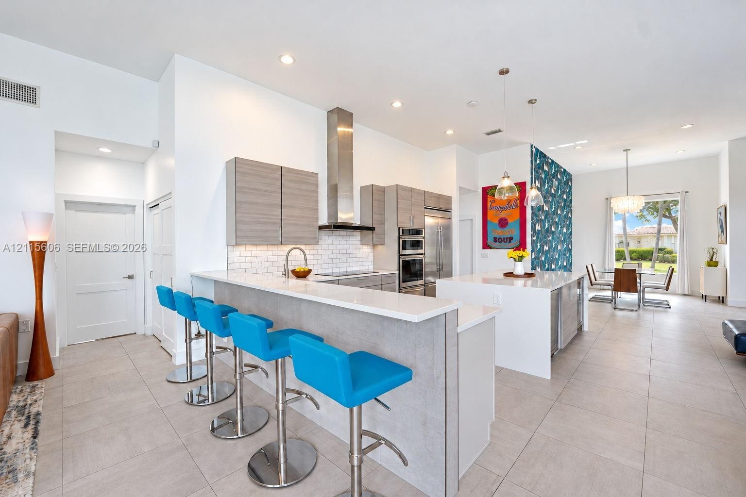 Kitchen featuring flat-panel cabinetry, a quartz-topped island with waterfall edge, stainless steel appliances, a white subway tile backsplash, and ov
