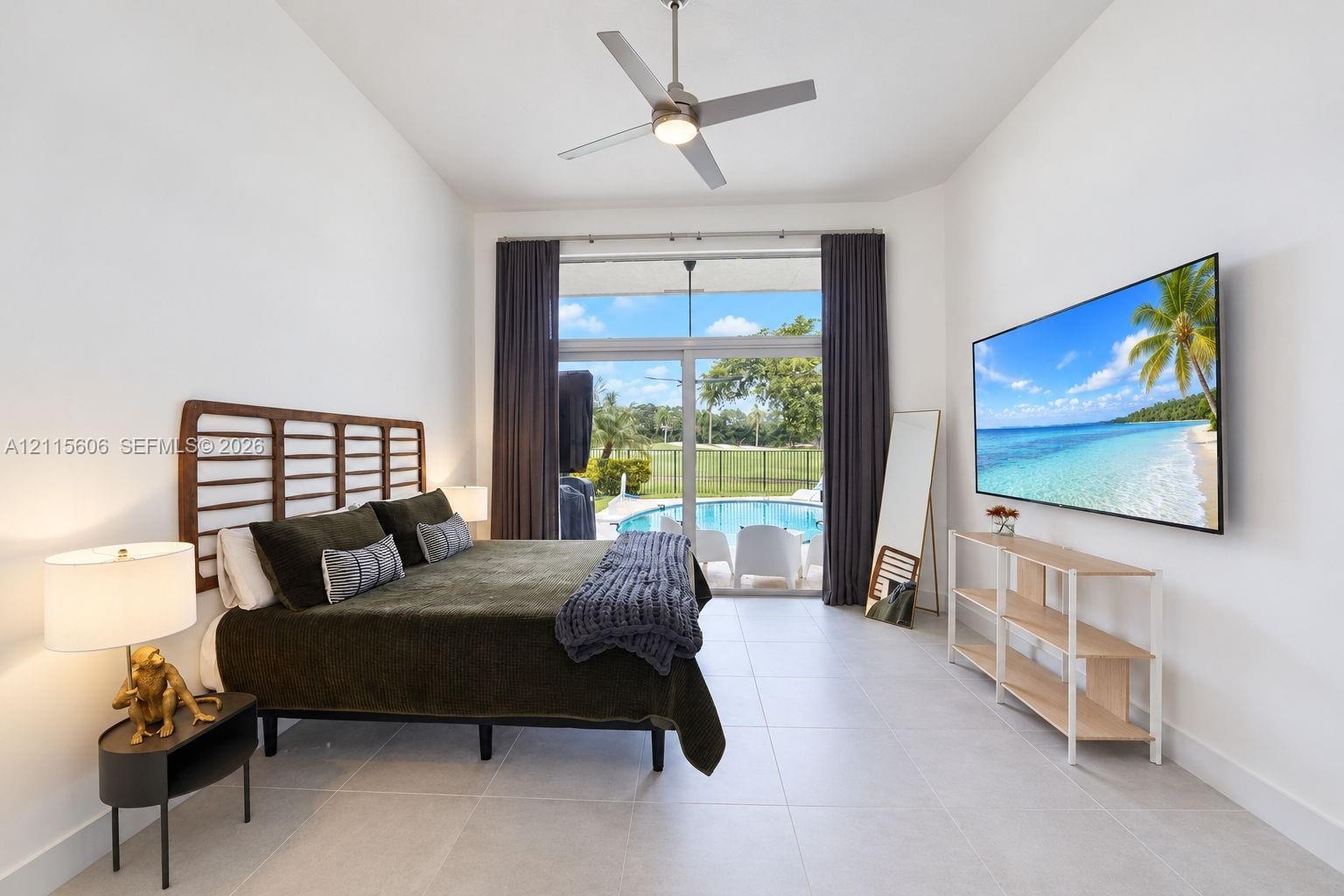 High-ceilinged room featuring large-format tile flooring, a brushed metal ceiling fan, and floor-to-ceiling sliding glass doors opening to an exterior