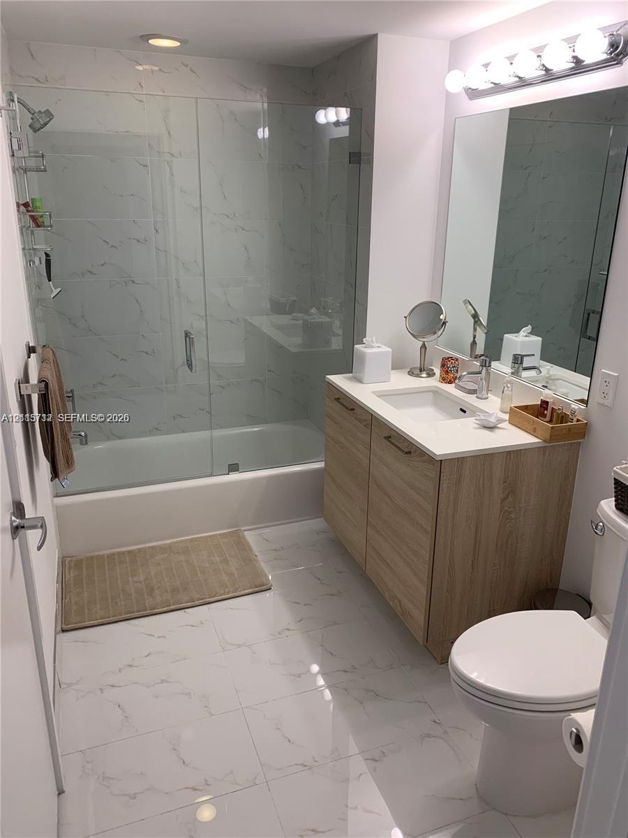 Bathroom featuring a wood-finish vanity, solid-surface countertop with integrated sink, glass-enclosed shower and tub combination with tile surround, 