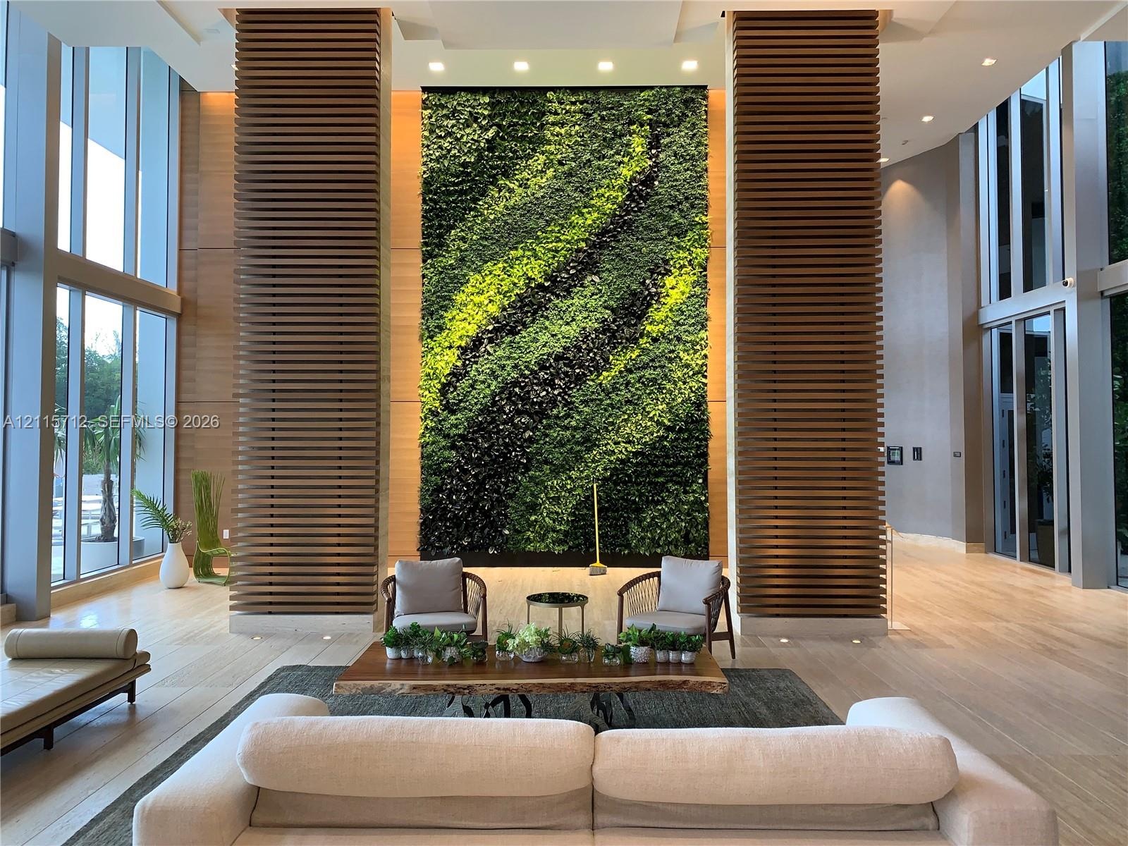 Grand entrance hall featuring floor-to-ceiling glass windows, dual floor-to-ceiling slatted wood columns, and a large-scale vertical living wall
