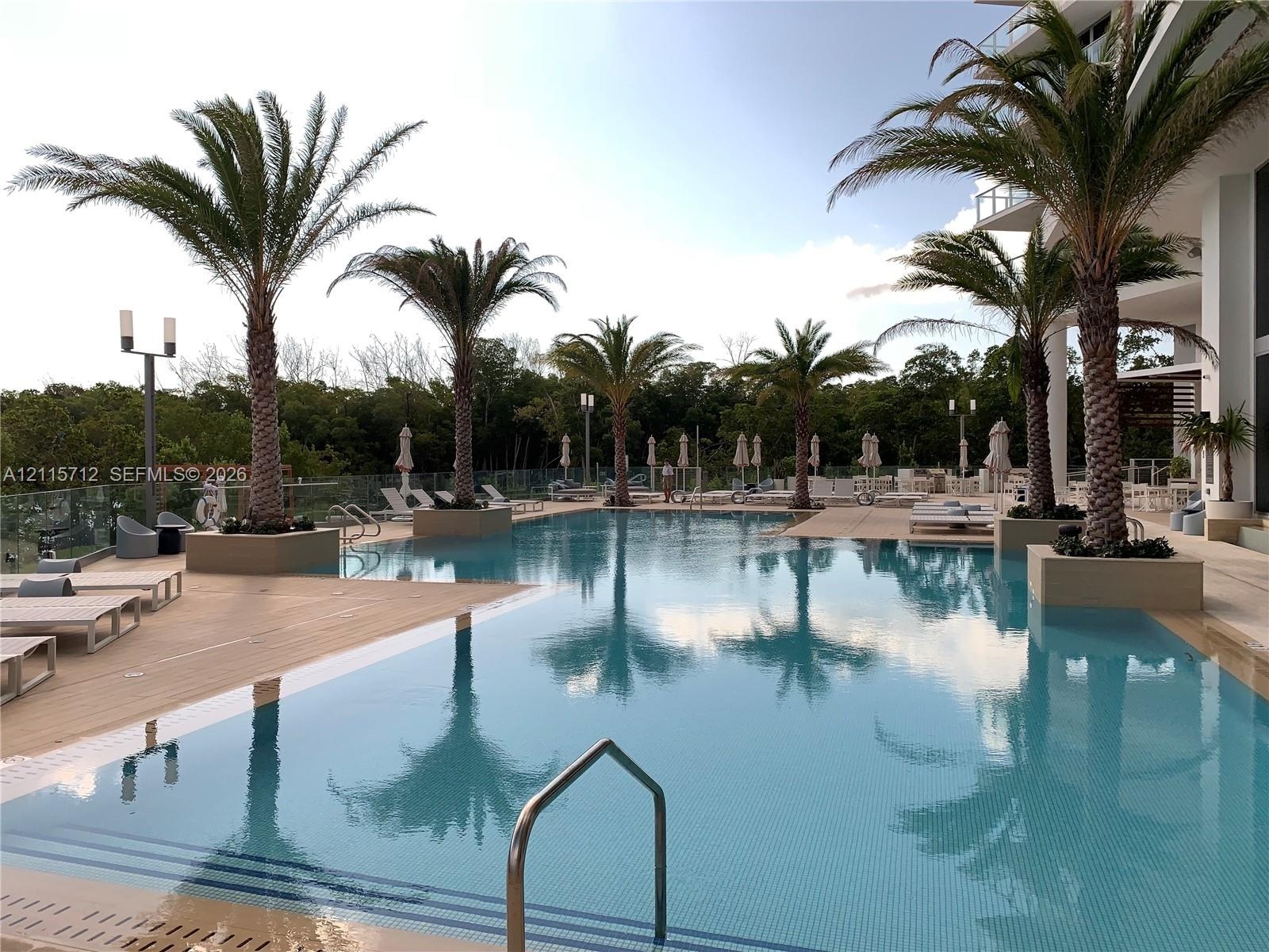In-ground pool with integrated palm tree planters, expansive wood-finish decking, and glass panel perimeter fencing