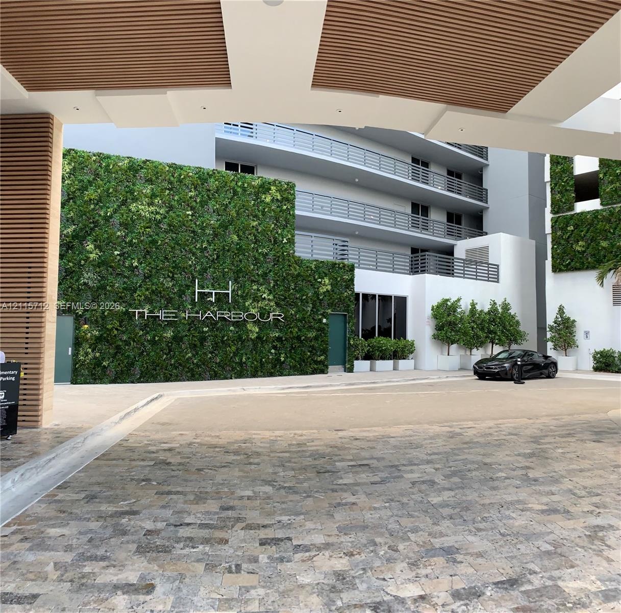Covered motor court featuring natural stone paving, architectural wood-slat ceiling detailing, a multi-story living green wall, and tiered balconies w