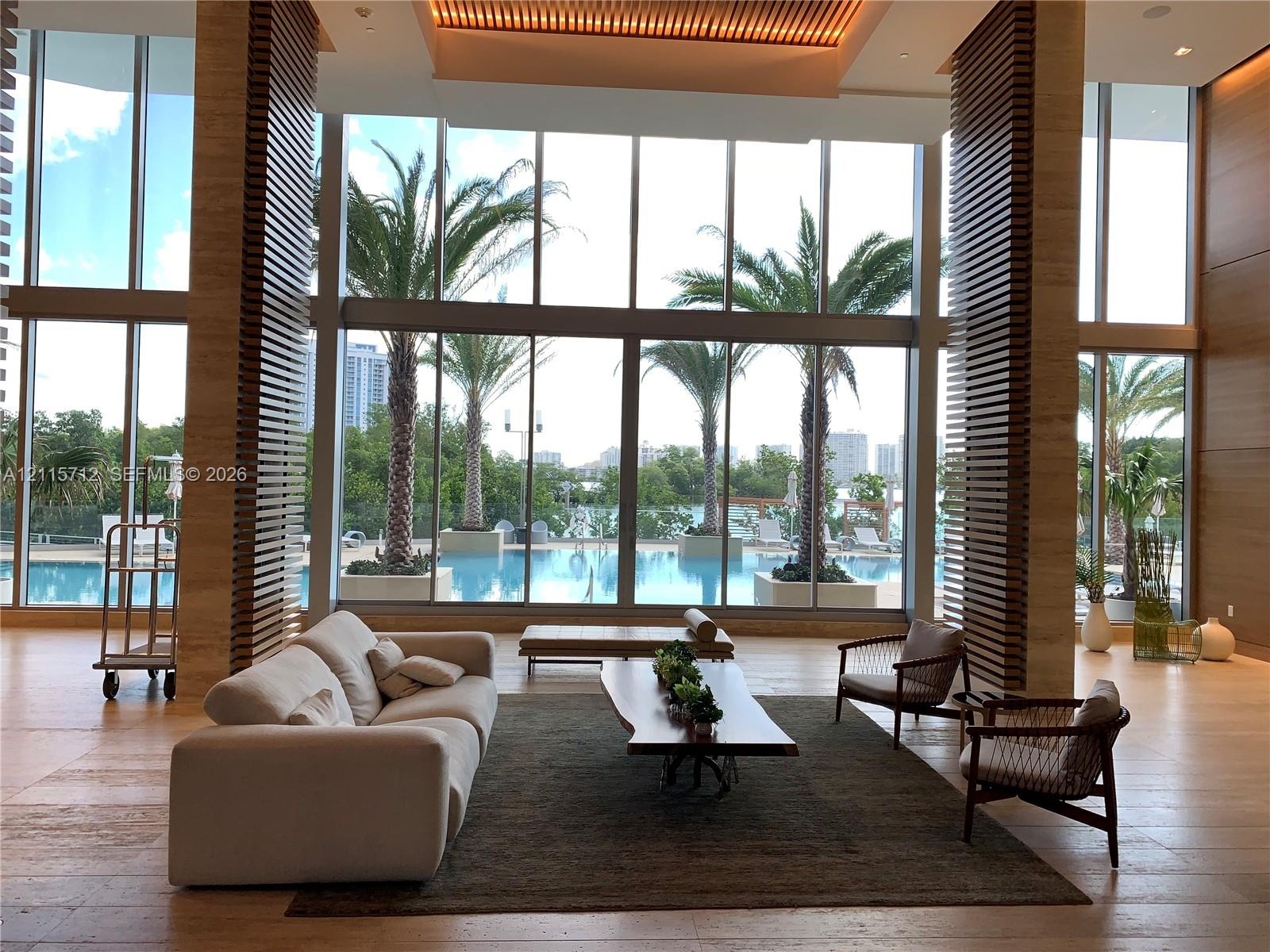 Double-height floor-to-ceiling windows, stone flooring, decorative slatted wood-finish columns, recessed architectural ceiling lighting, and exterior 