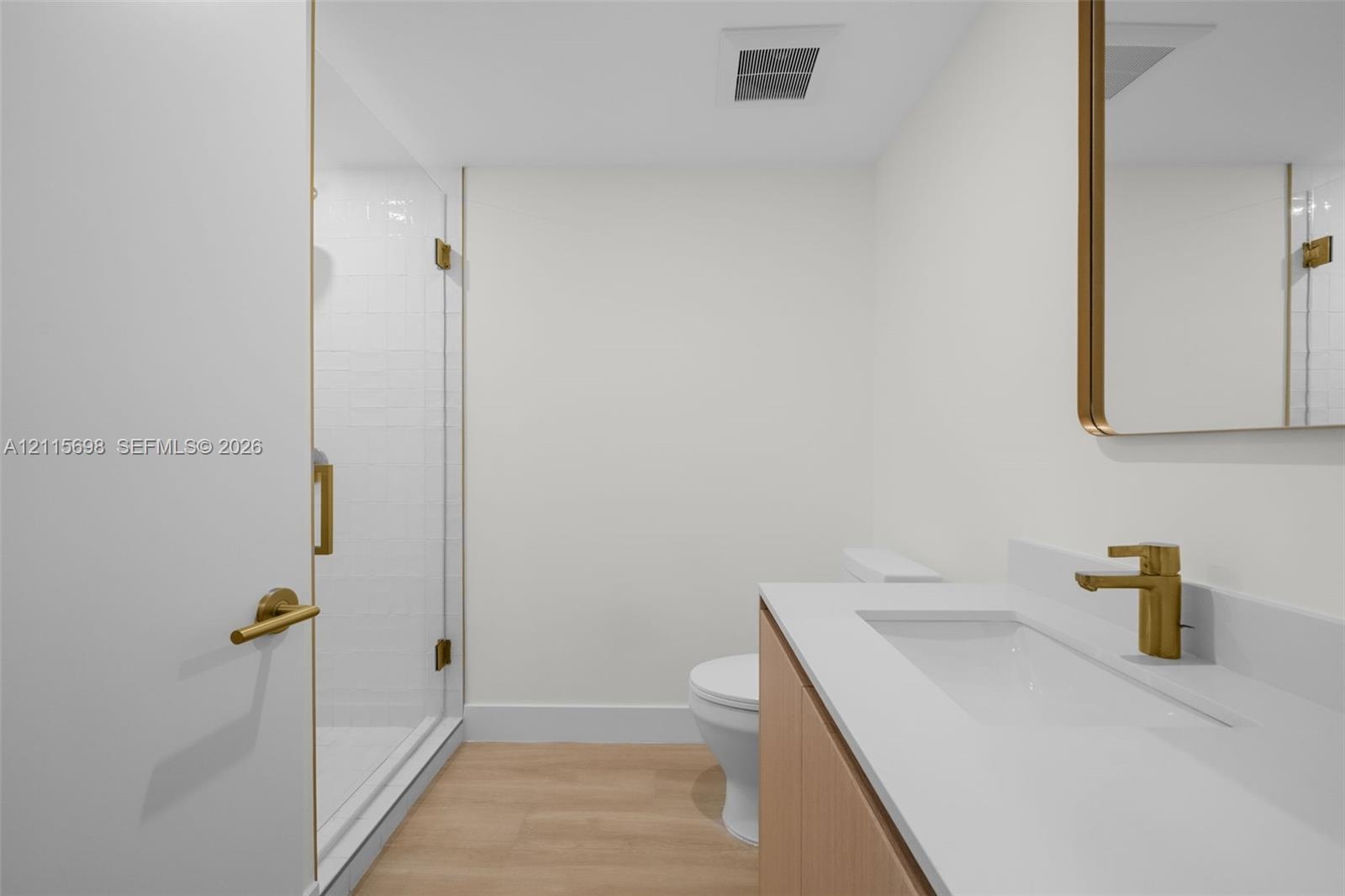 Guest bathroom featuring a walk-in shower with a glass enclosure, wood-finish flooring, vanity with a white countertop and integrated sink, brass-tone