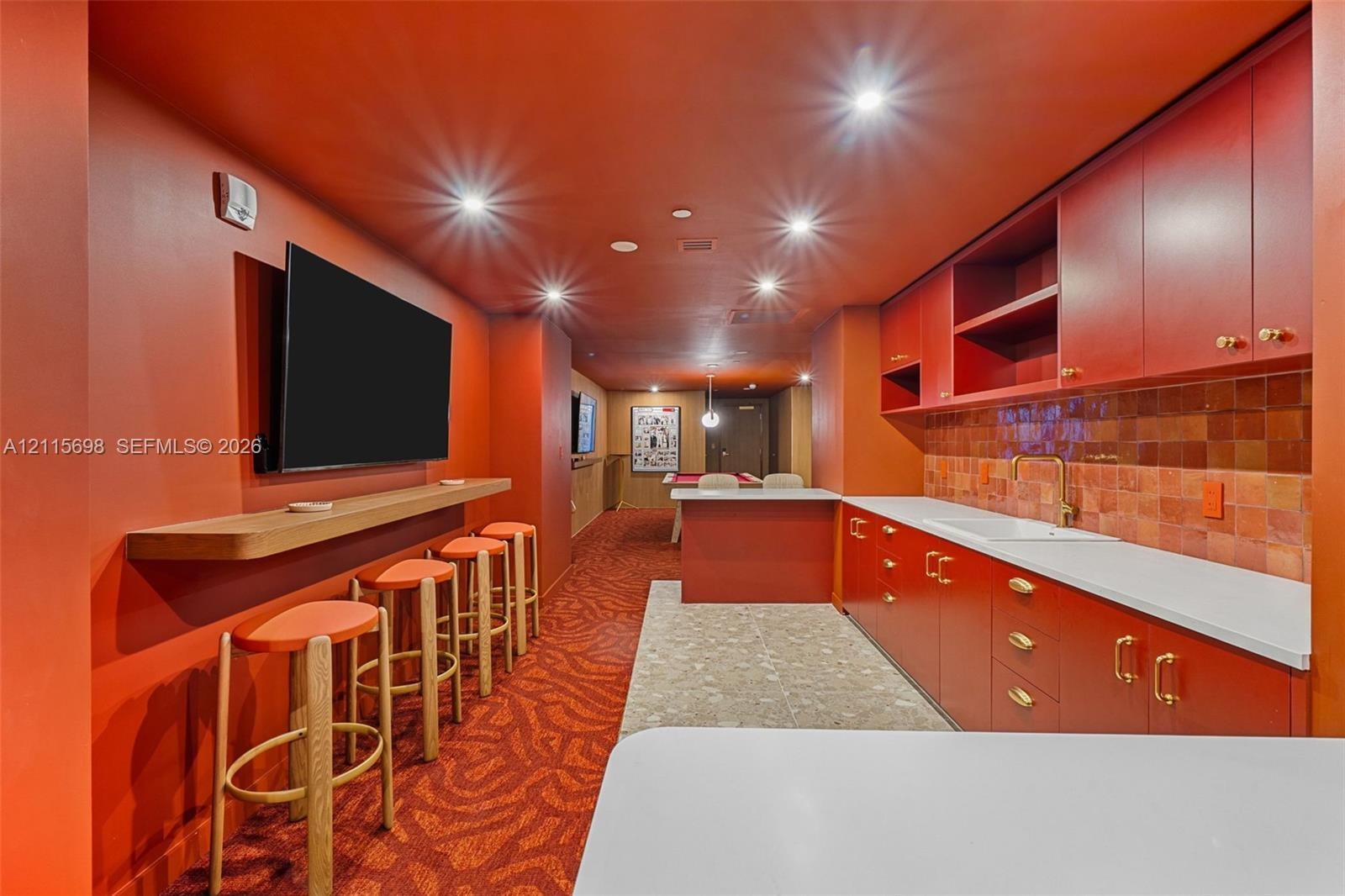 Building Amenity room with built-in cabinetry with brass-finish hardware, integrated sink, tile backsplash, countertop seating, and recessed ceiling l