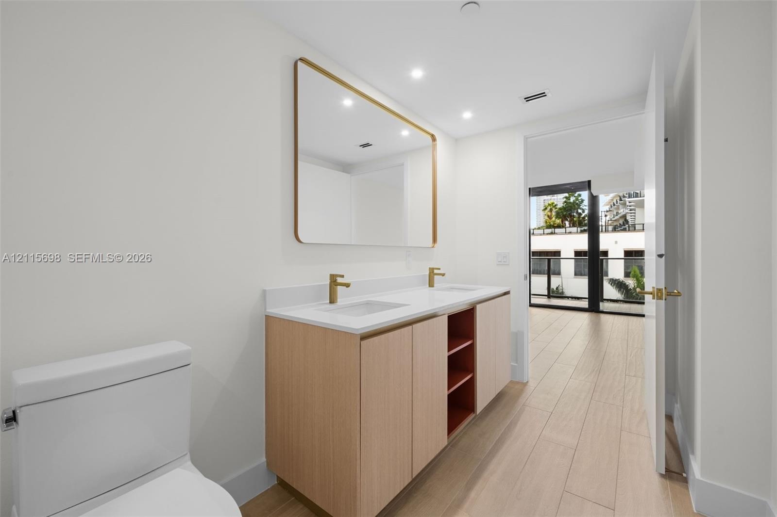 Master bathroom Dual-sink vanity with light wood cabinetry, white stone countertop, rectangular undermount sinks, and gold-tone fixtures, complemented