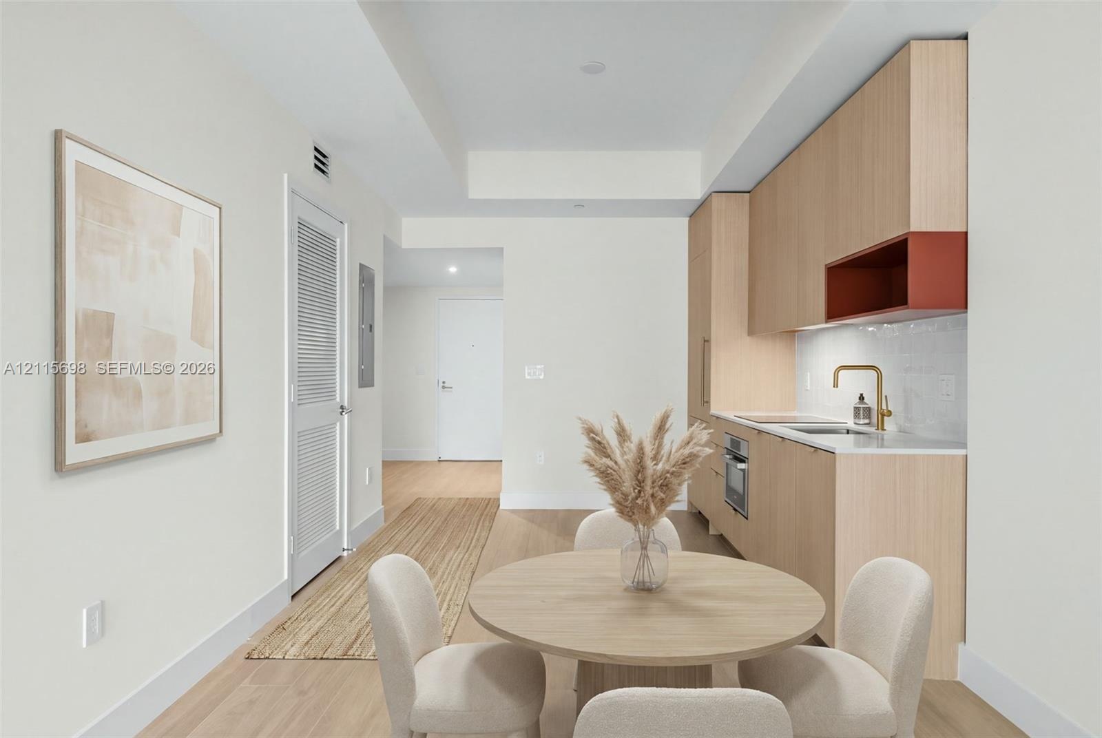 Kitchen featuring light wood-finish cabinetry, an integrated cooktop, a built-in oven, a brass-tone faucet, and a stone-finish countertop - staged