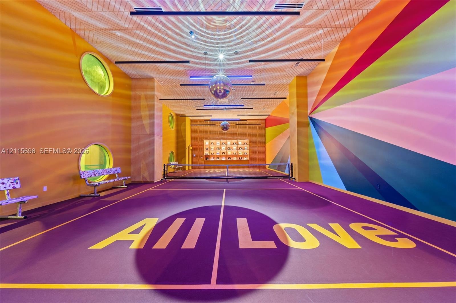Indoor pickle ball court featuring a high-contrast athletic surface, circular windows, linear ceiling lighting, mirrored spherical pendants, and custo