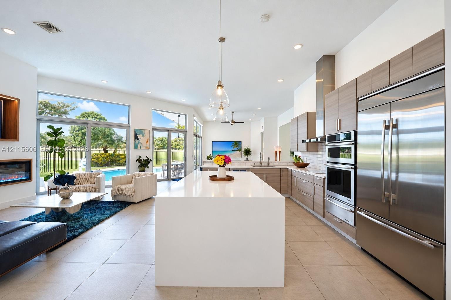 Open-concept interior featuring large center island with solid-surface countertop, linear wood-finish cabinetry, stainless steel built-in appliances, 