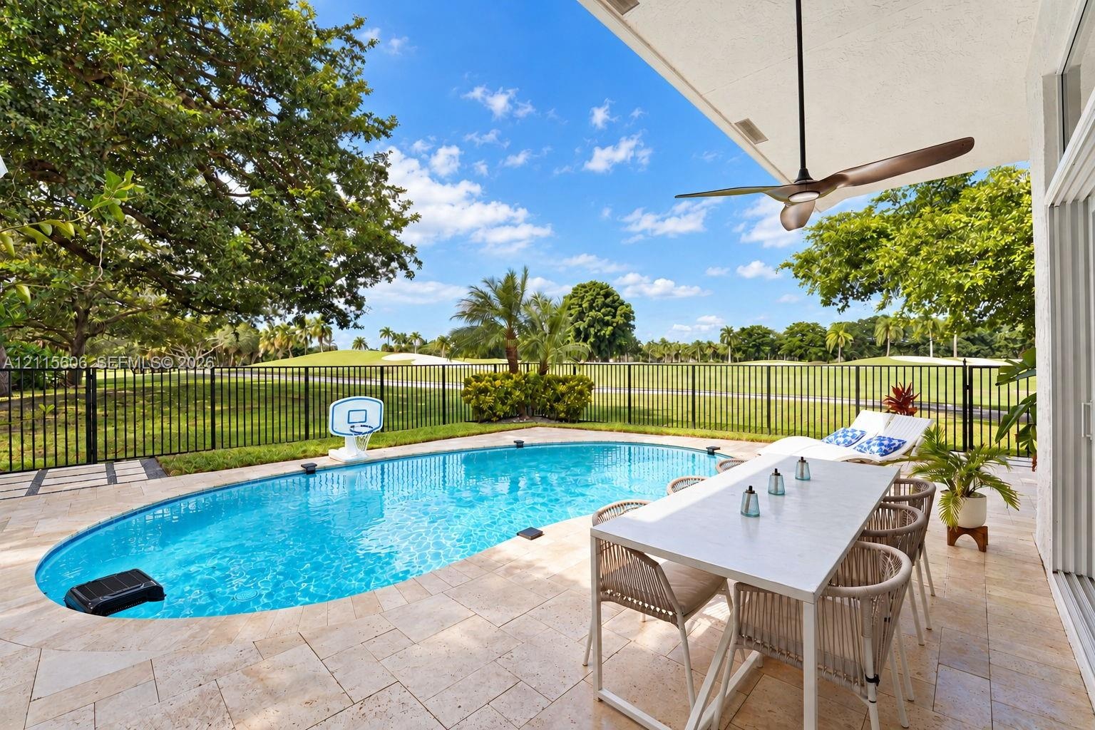 Covered patio featuring a ceiling fan, stone-tile flooring, an in-ground pool, and metal perimeter fencing