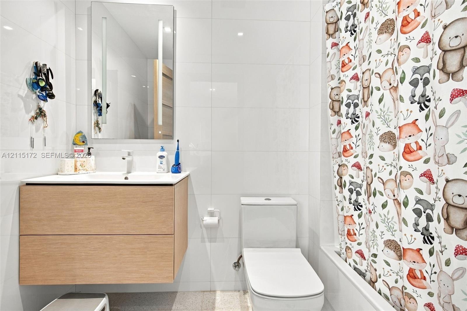 Floating vanity with wood-finish cabinetry, integrated rectangular sink, wall-mounted LED-backlit mirror, and full-height white wall tiling