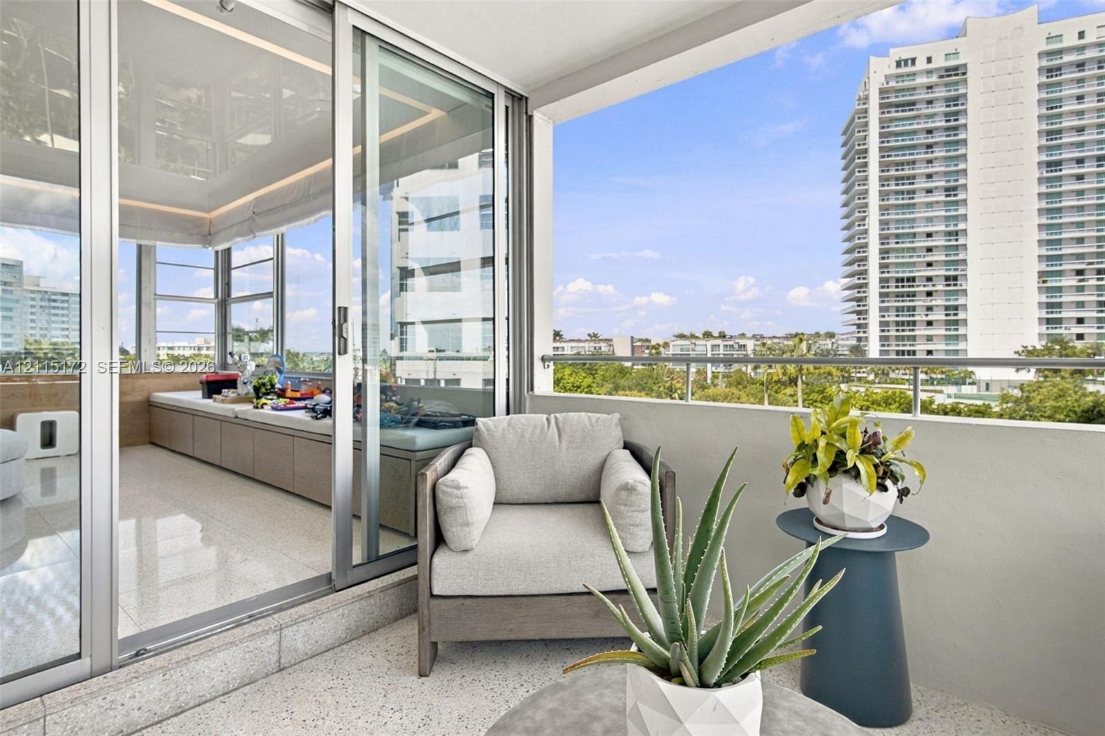 Covered balcony with a metal railing and light-colored flooring, accessed via floor-to-ceiling glass sliding doors