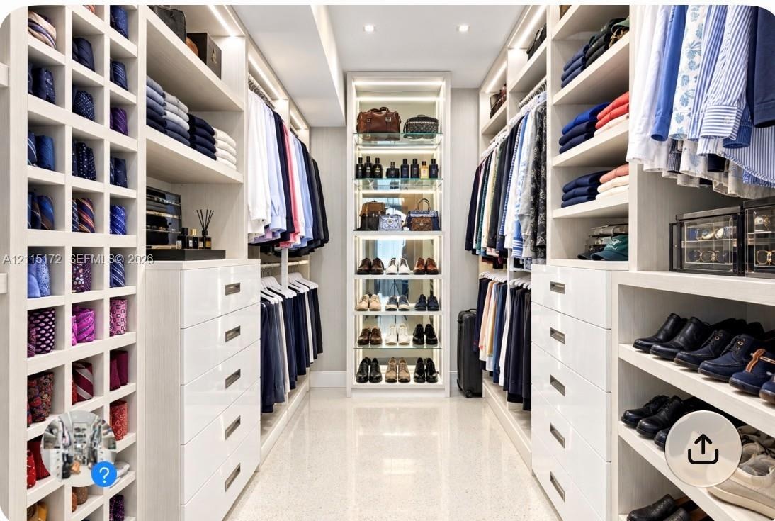 Custom dressing area featuring extensive white built-in cabinetry, floor-to-ceiling storage cubbies, integrated accent lighting, and polished stone fl