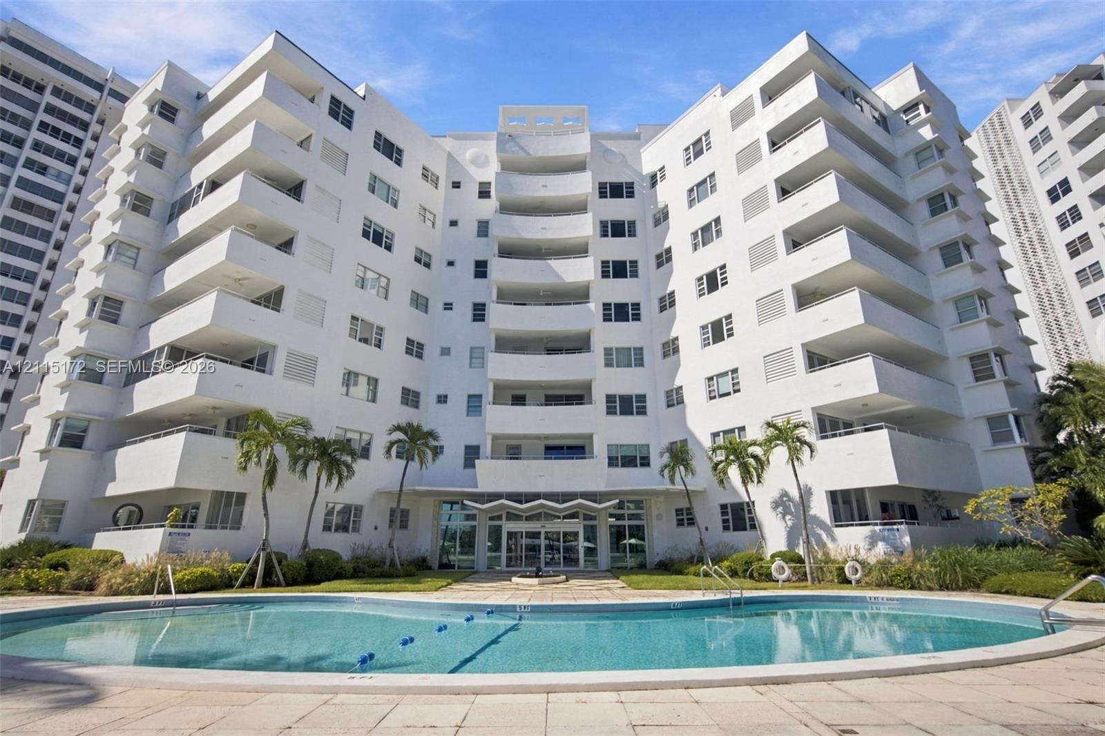 Mid-rise residential building featuring stacked private balconies, a ground-level swimming pool, and stone-paved pool deck