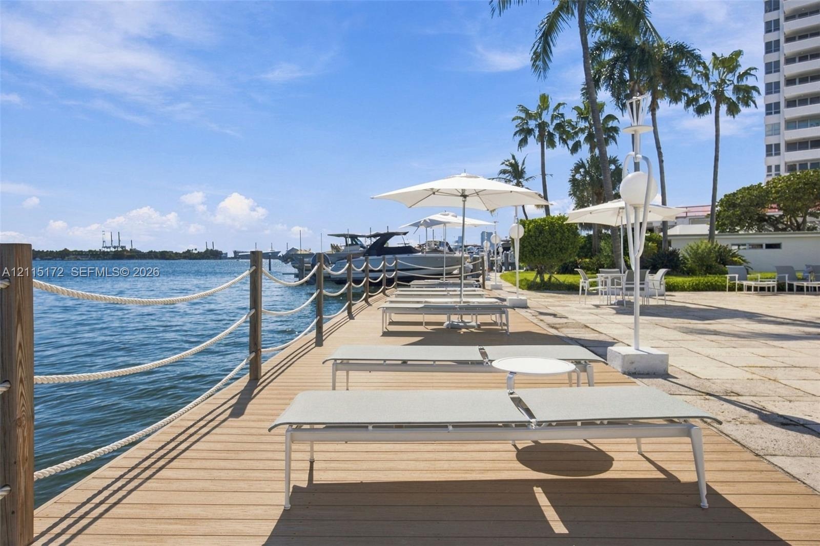 Waterfront deck featuring wood-finish decking, rope railing, stone-paved patio area, and mature palm trees