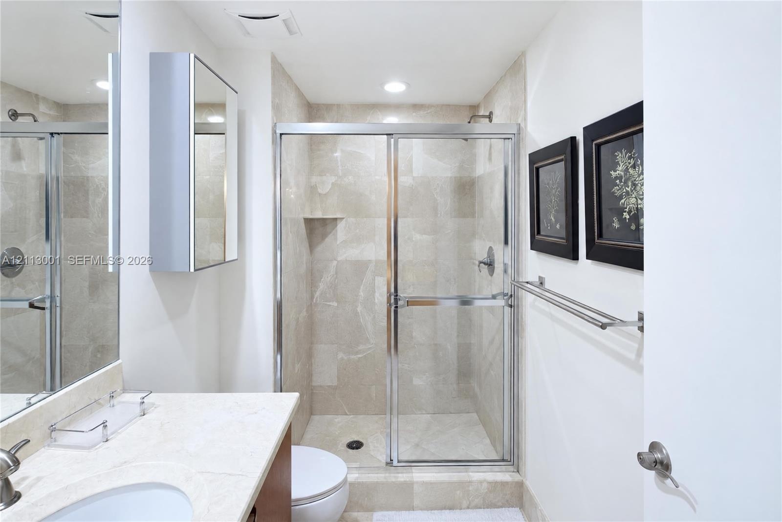 Bathroom featuring a walk-in shower with stone tile surround, chrome sliding glass enclosure, stone countertop vanity, recessed lighting, and a mirror