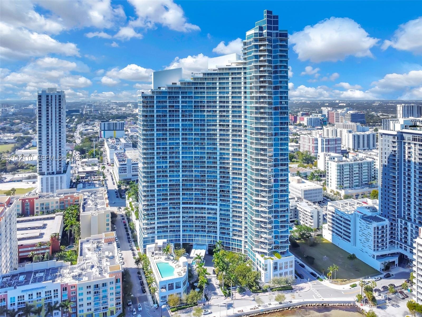 High-rise building featuring a glass facade, expansive private balconies, a ground-level swimming pool, and proximity to the waterfront
