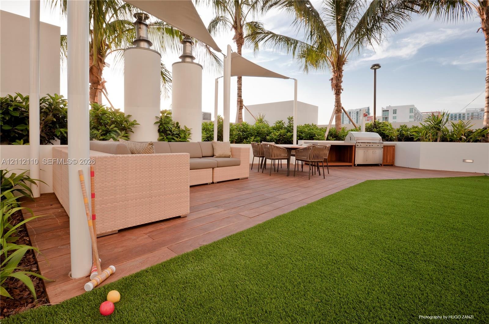 Outdoor terrace featuring wood-finish decking, integrated stainless steel grill station, synthetic turf lawn, architectural shade sails, and perimeter