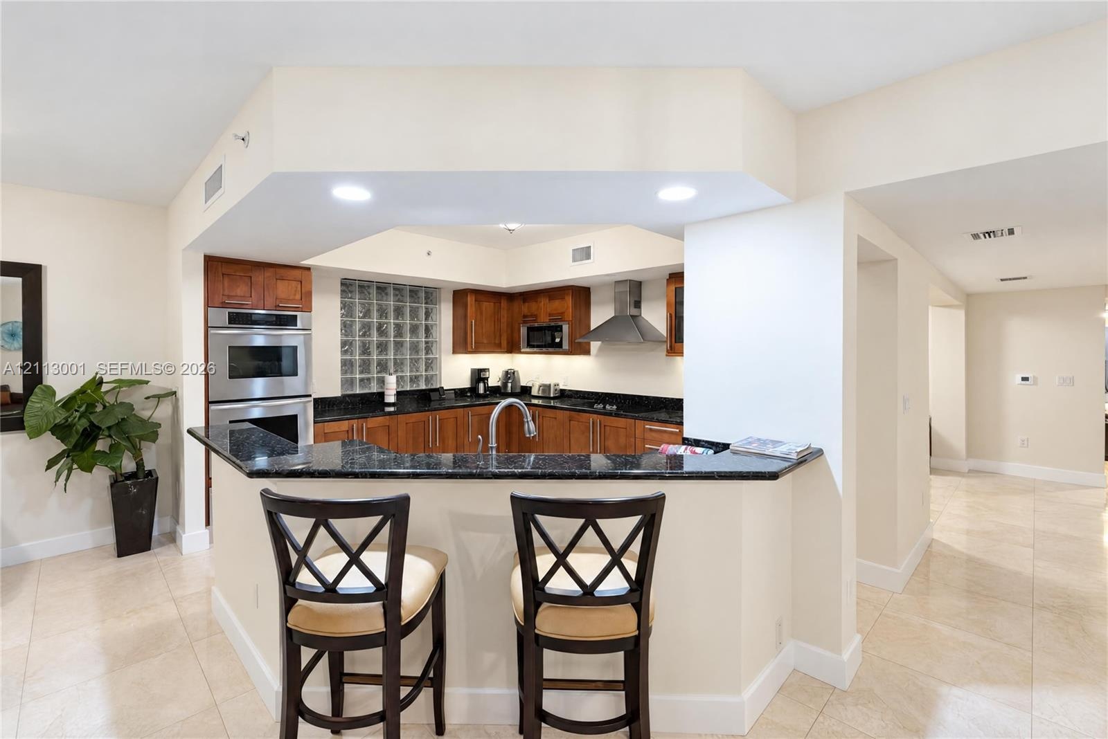 Kitchen featuring wood cabinetry, stone countertops, glass block accent window, stainless steel double wall oven, and recessed lighting